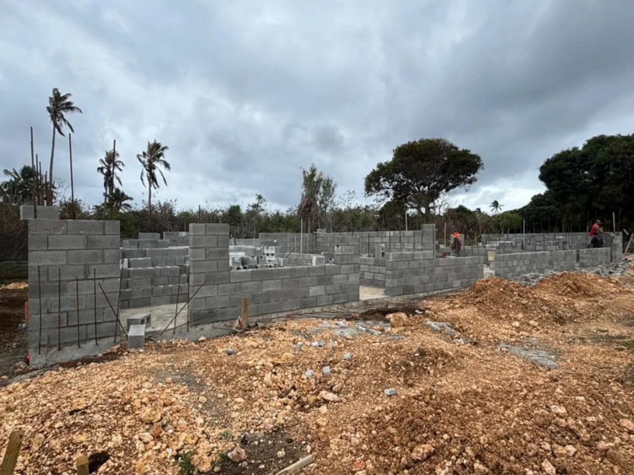 Construction site with partially built concrete block walls, dirt, and overcast sky.