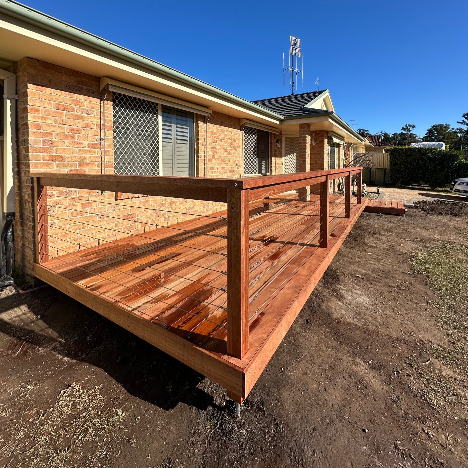 A newly built wooden deck attached to a brick house. The deck features a custom made step to allow easy access to the deck and hand railings for safety. The client was extremely happy with the end product.