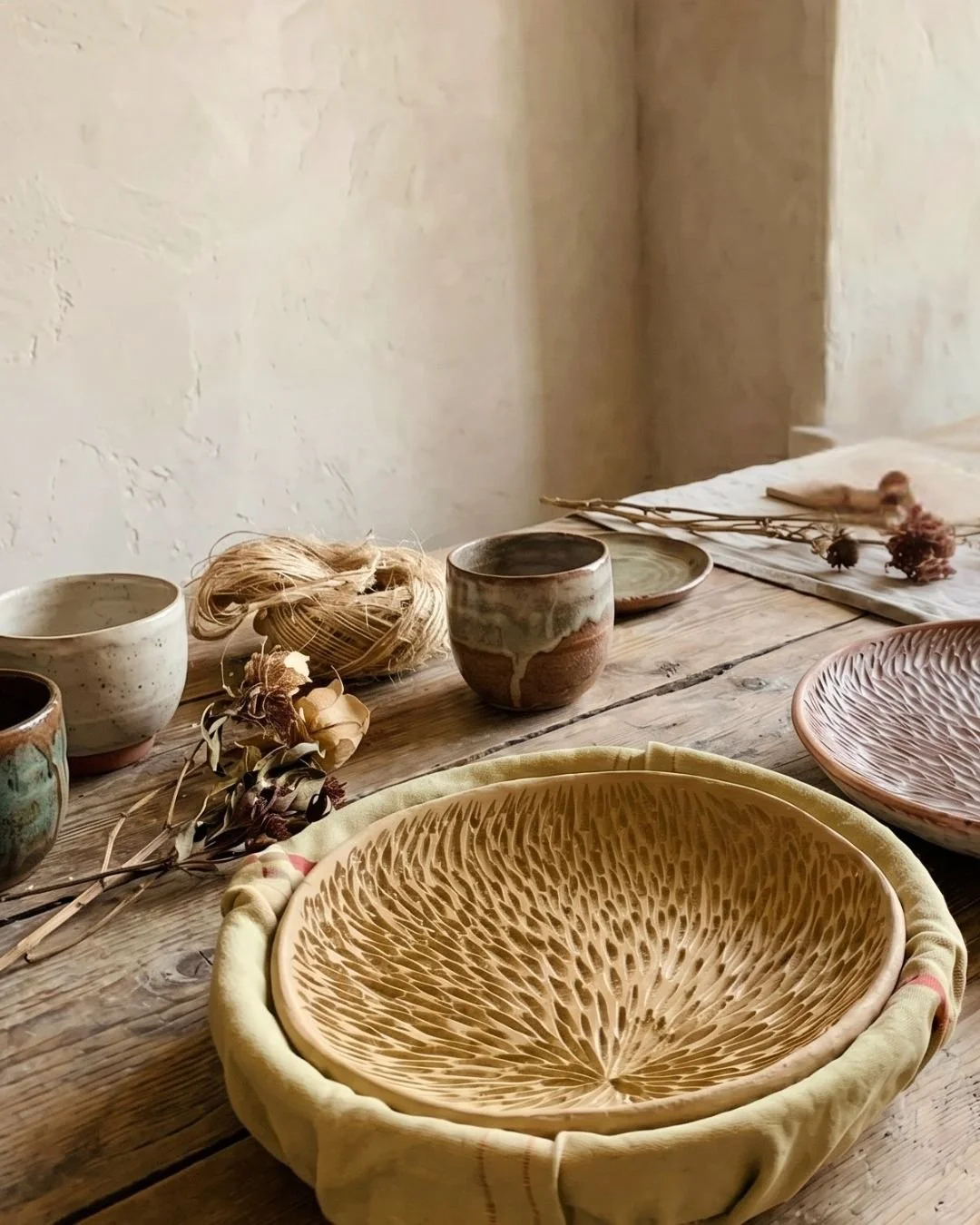 Blumen und Keramikschalen auf einem Holztablett, rustikaler Holztisch im Raum, natürlicher Lichteinfall, minimalistische Dekoration, Deko-Objekte und Trockengefäße