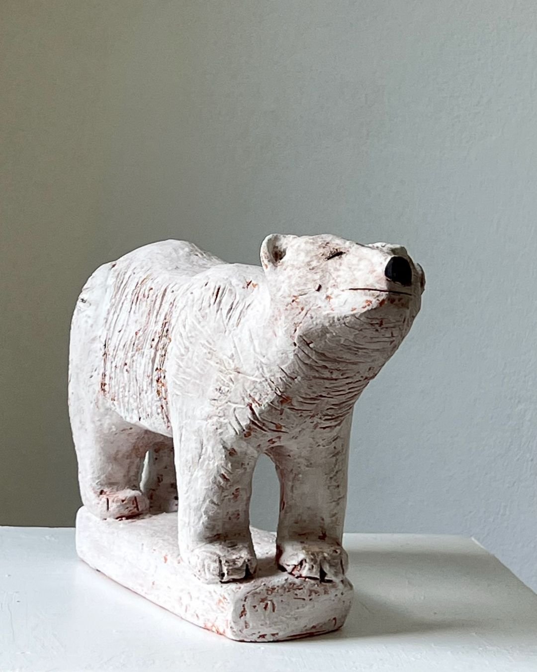 Weiße Tierfigur, die einen Bären darstellt, auf einem weißen Tisch vor einem neutralen Hintergrund.