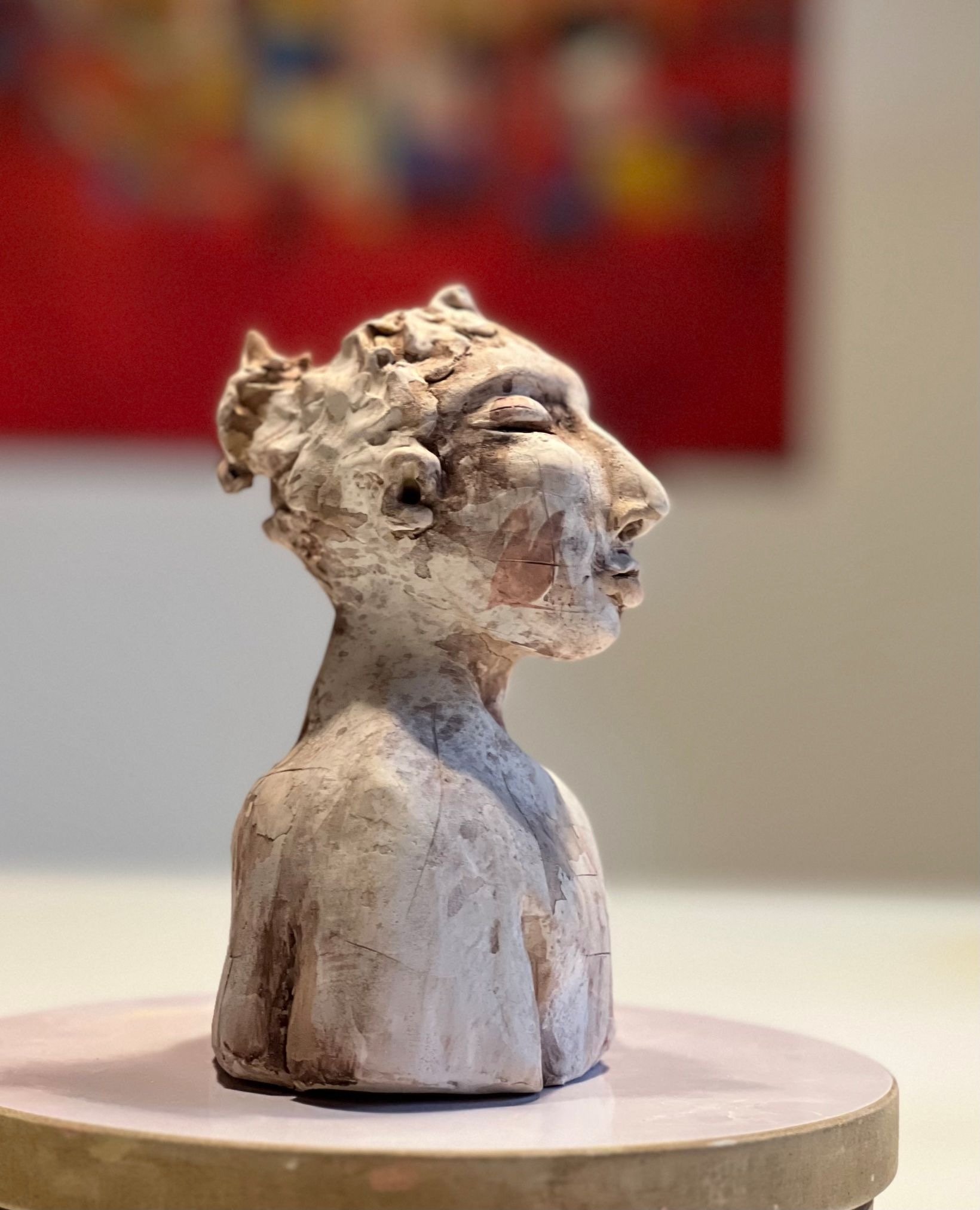 Skulptur einer weiblichen Figur aus Holz mit stilisierten, abstrakten Merkmalen, auf einem runden weißen Sockel
