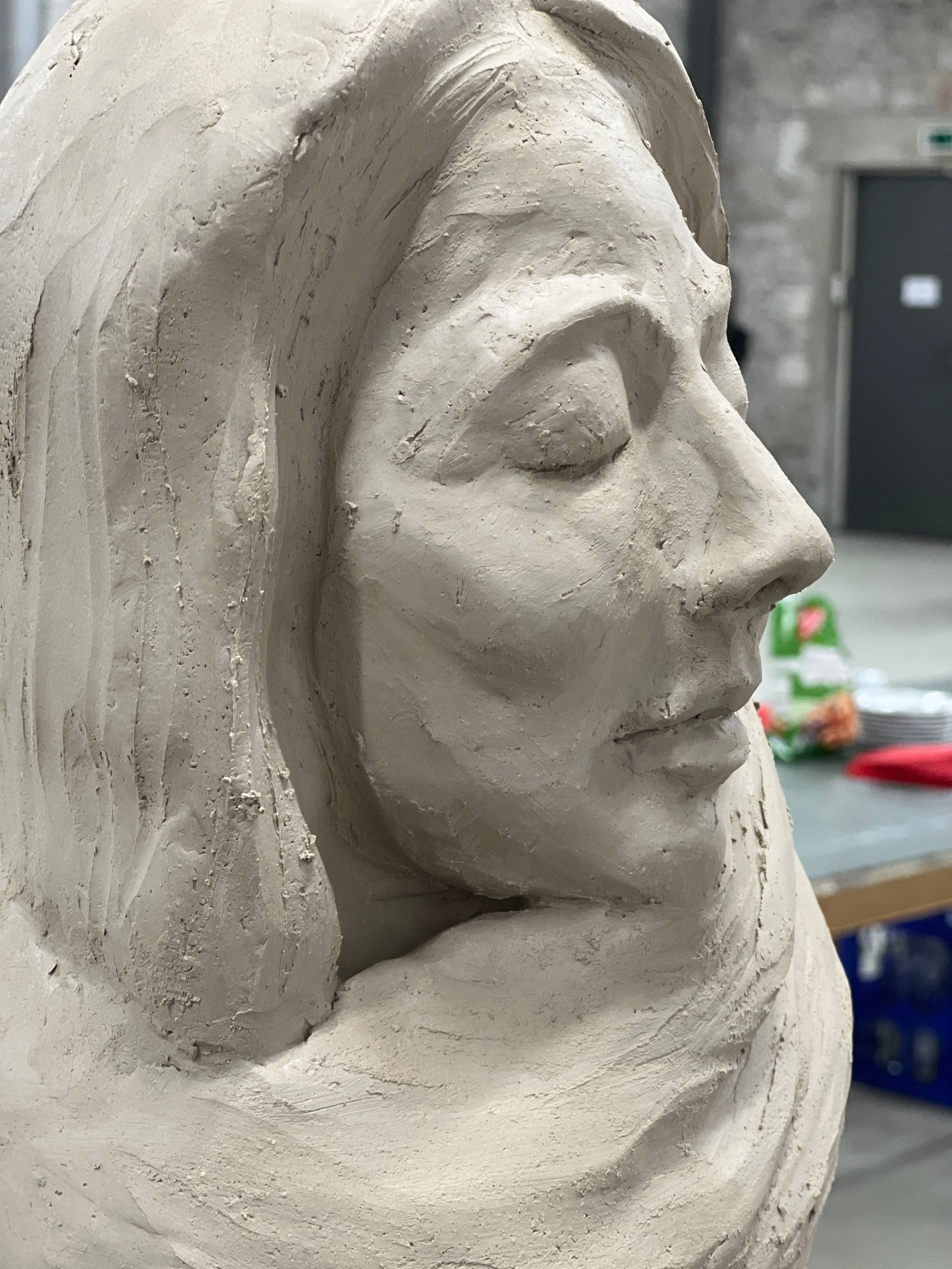 Eine detaillierte Skulptur eines menschlichen Gesichts, wahrscheinlich aus Ton oder Gips, in einem Atelier oder Werkstattumfeld.