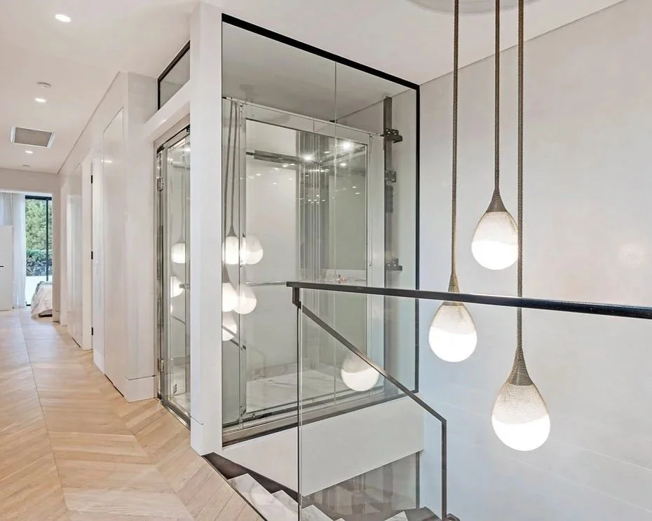 Modern interior hallway with a glass-enclosed elevator and hanging pendant lights.