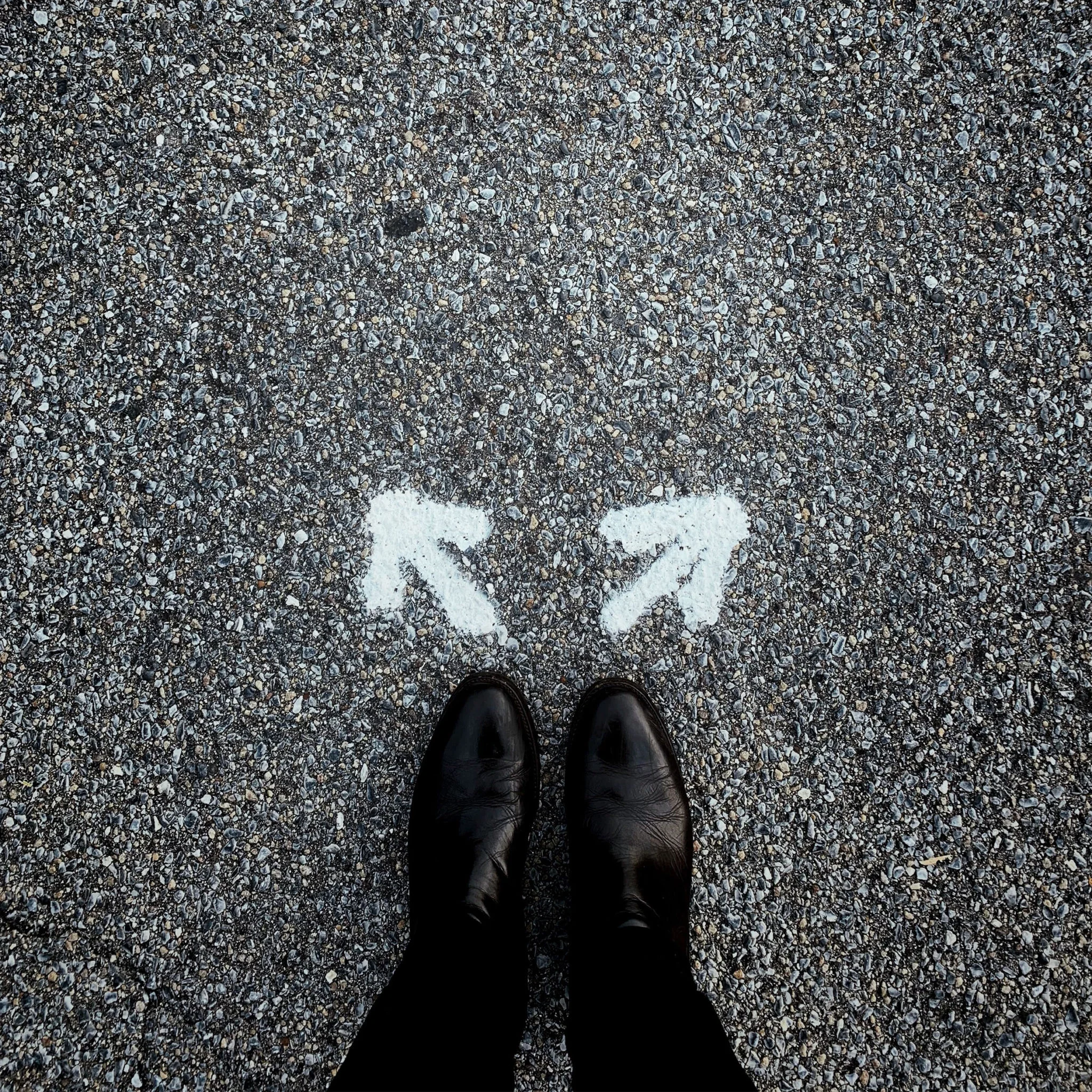 Perspectives des chaussures noires sur un sol de gravier et un point blanc peint sur le sol. La photo est prise depuis la personne qui porte les chaussures.