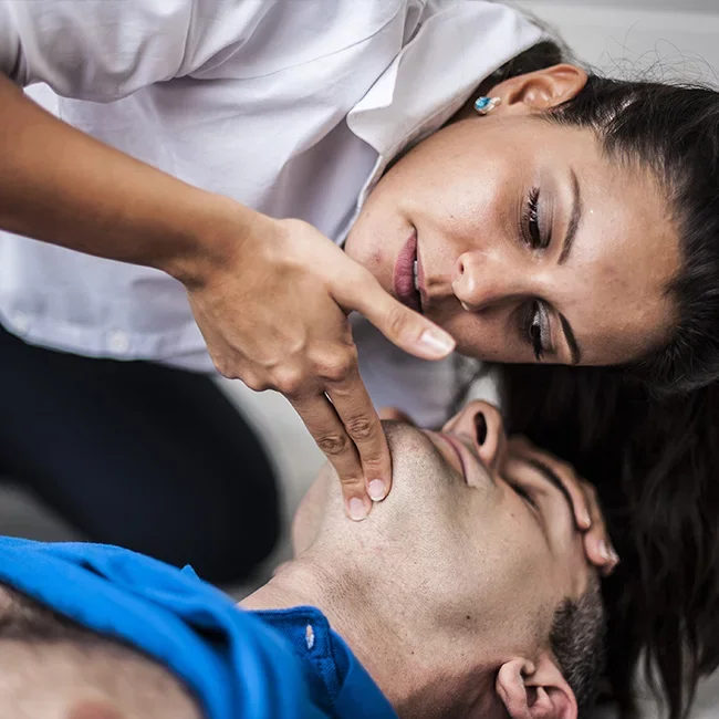 Une femme pratiquant une réanimation cardiorespiratoire sur un homme allongé sur le sol.