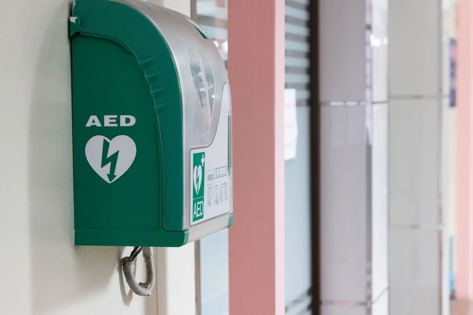 Distributeur automatique de défibrillateur AED vert fixé au mur dans un bâtiment public.