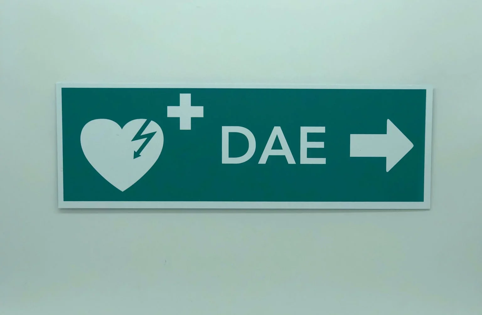 Panneau de direction indiquant un défibrillateur automatisé externe (DAE) avec une icône de cœur avec un éclair, une croix blanche, le texte 'DAE', et une flèche pointant vers la droite.