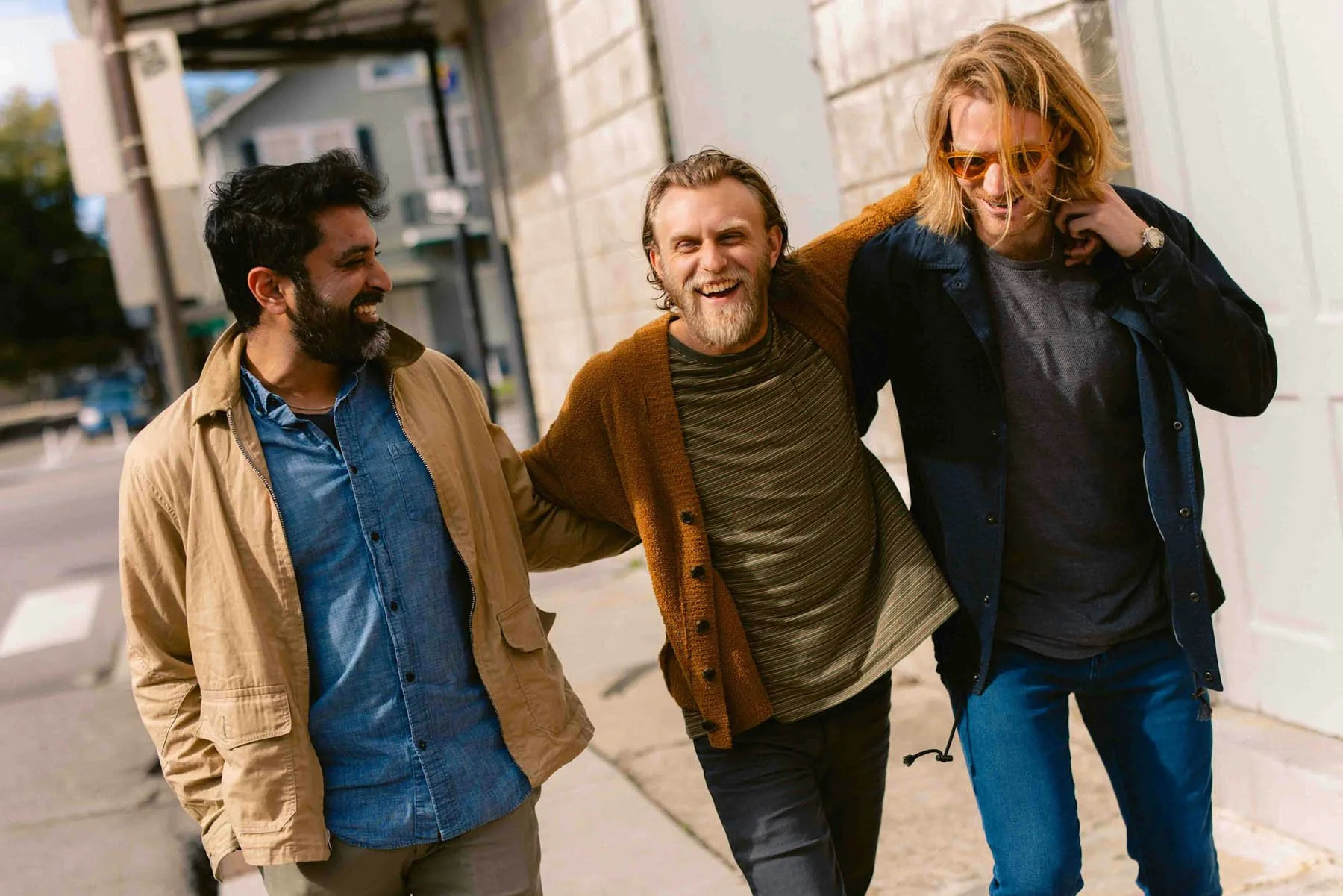 Three men walking together on a city sidewalk, smiling and enjoying each other's company.
