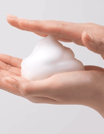 Hands holding a soft, white foam or whipped cream in a minimalist setting.