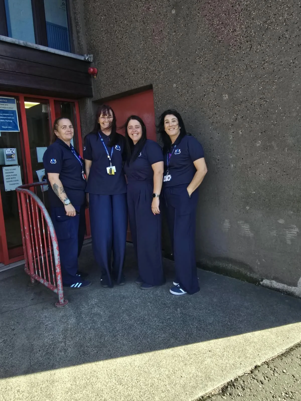 Four women in matching navy blue uniforms standing together outside a building. They are smiling and posing for the photo.