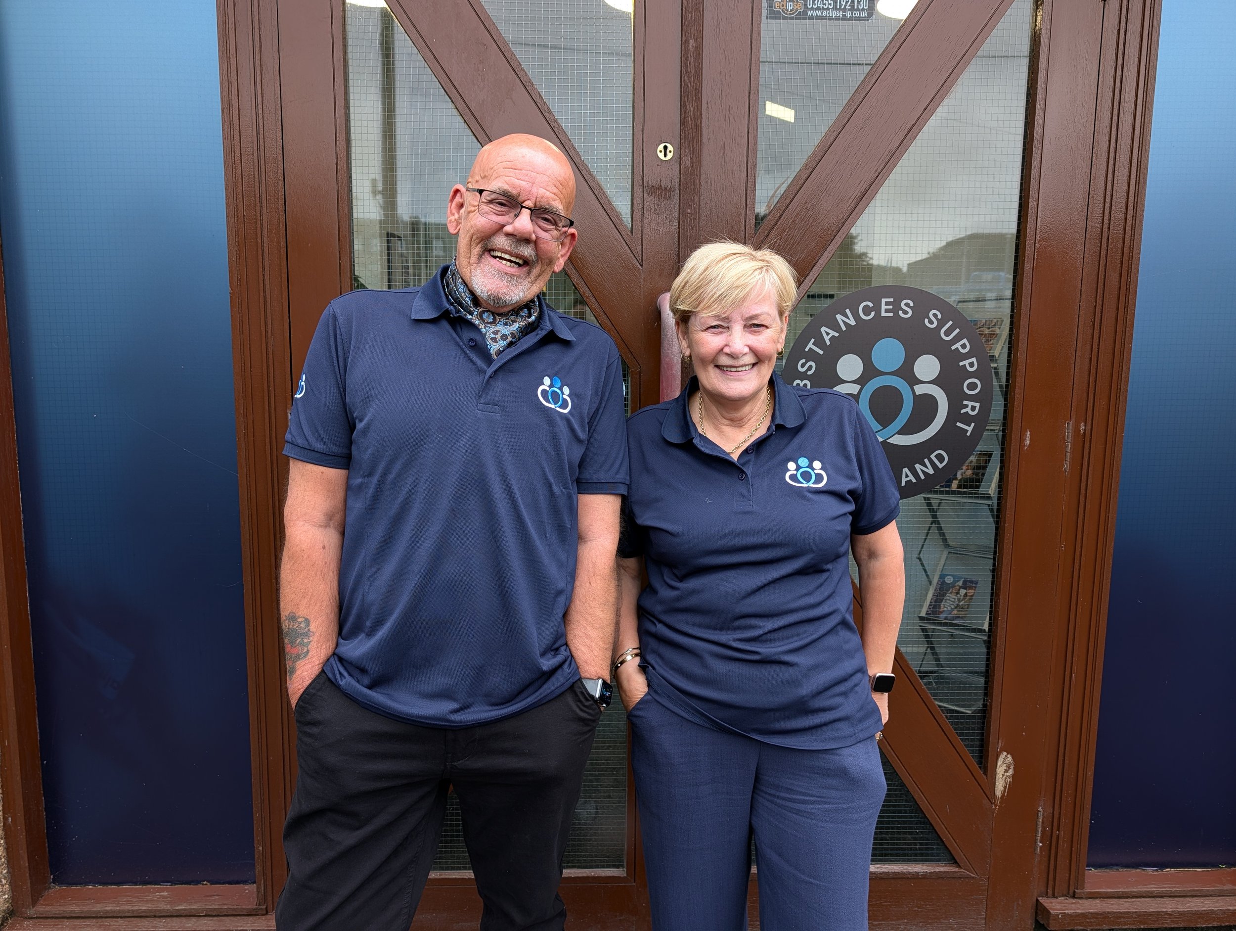 Two trainers standing in front of building. Woman and man, smiling.