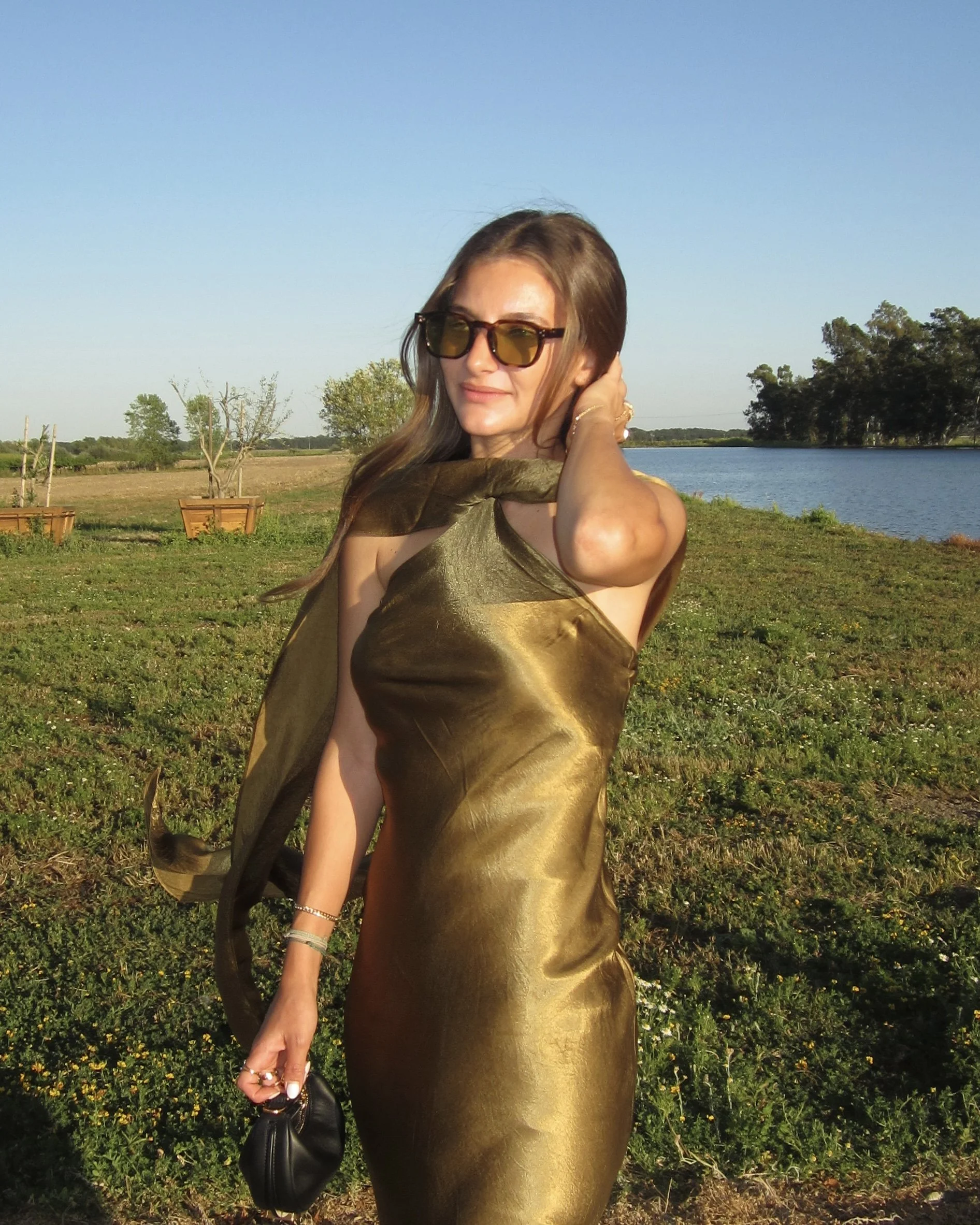 Woman in a gold dress and sunglasses outdoors near a river