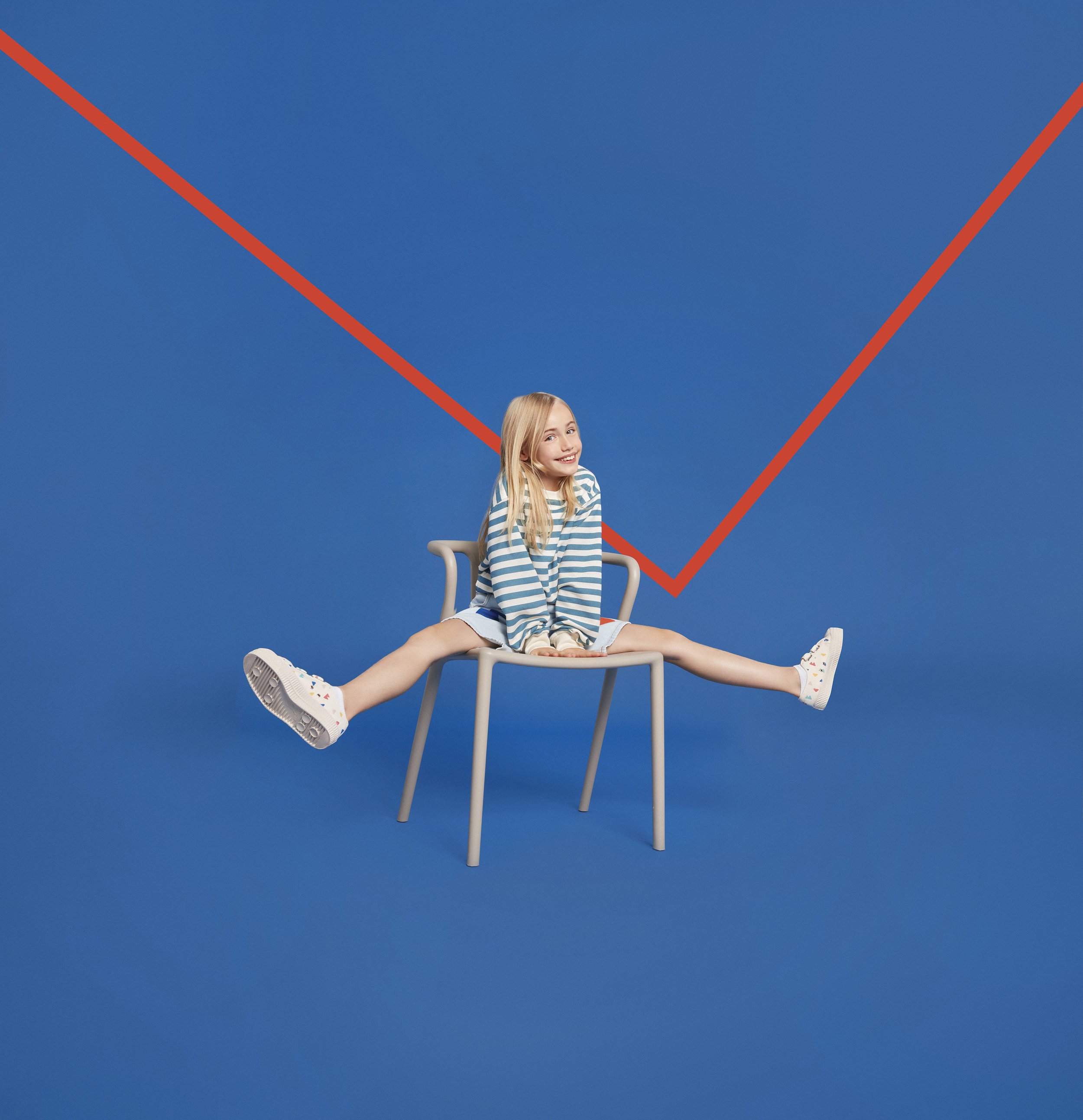 Une femme assise sur une chaise, esquissant un sourire, avec un fond bleu. La photo est teintée de bleu et met en avant la femme et la chaise, avec un décor minimaliste.