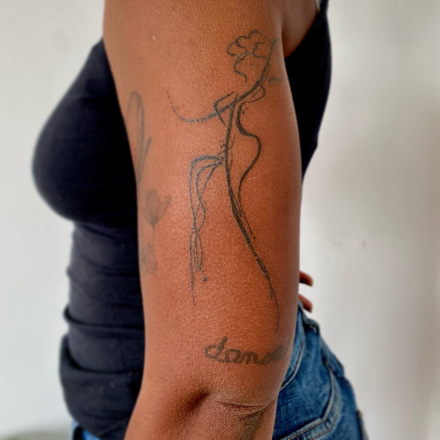 Tatouage en ligne d'une femme. Le tatouage inclut une figure féminine stylisée, une fleur.