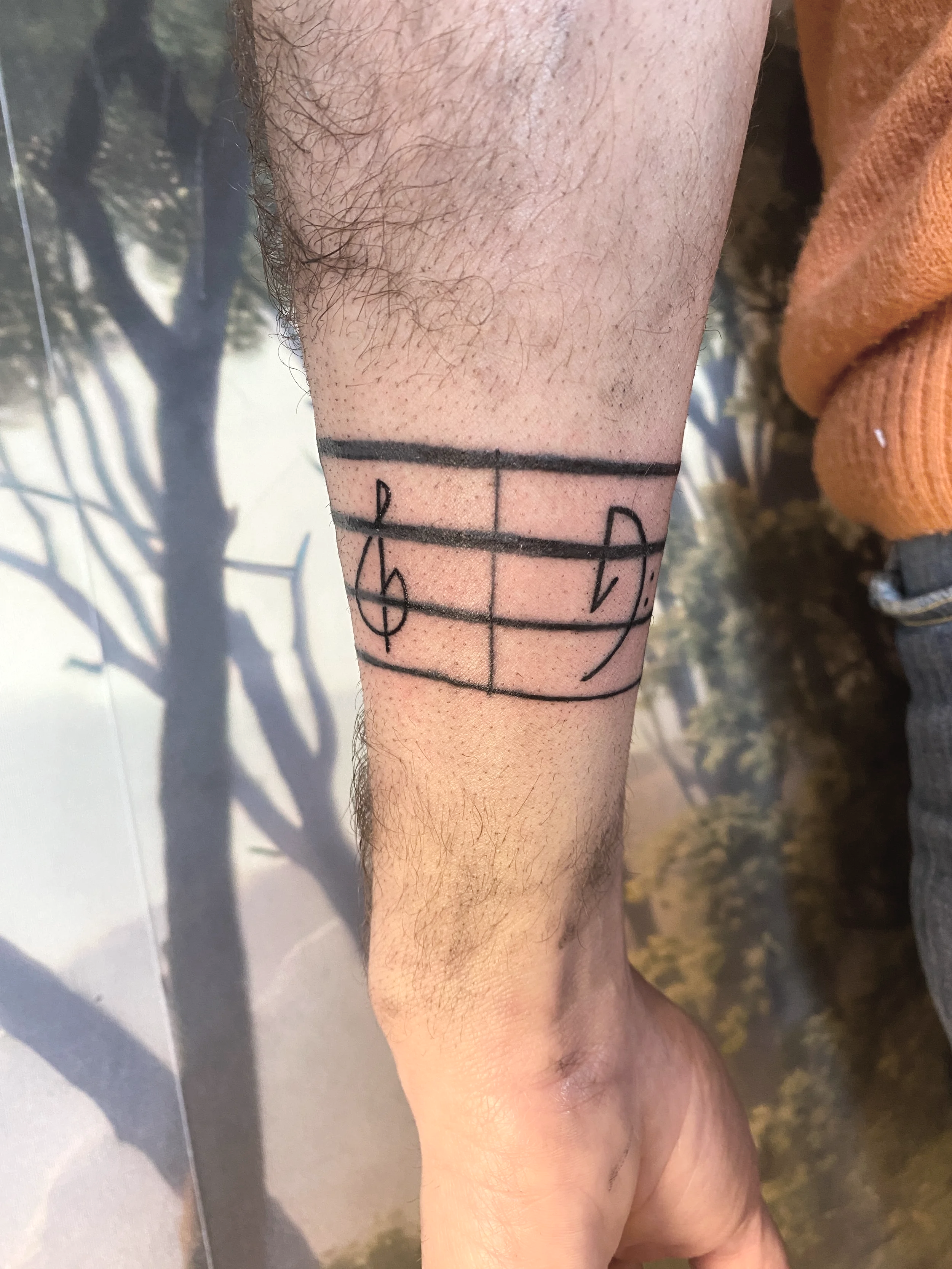 Un avant-bras humain avec un tatouage représentant une portée musicale. Le tatouage est noir, dessiné sur la peau claire, avec des lignes de portée et des notes de musique.