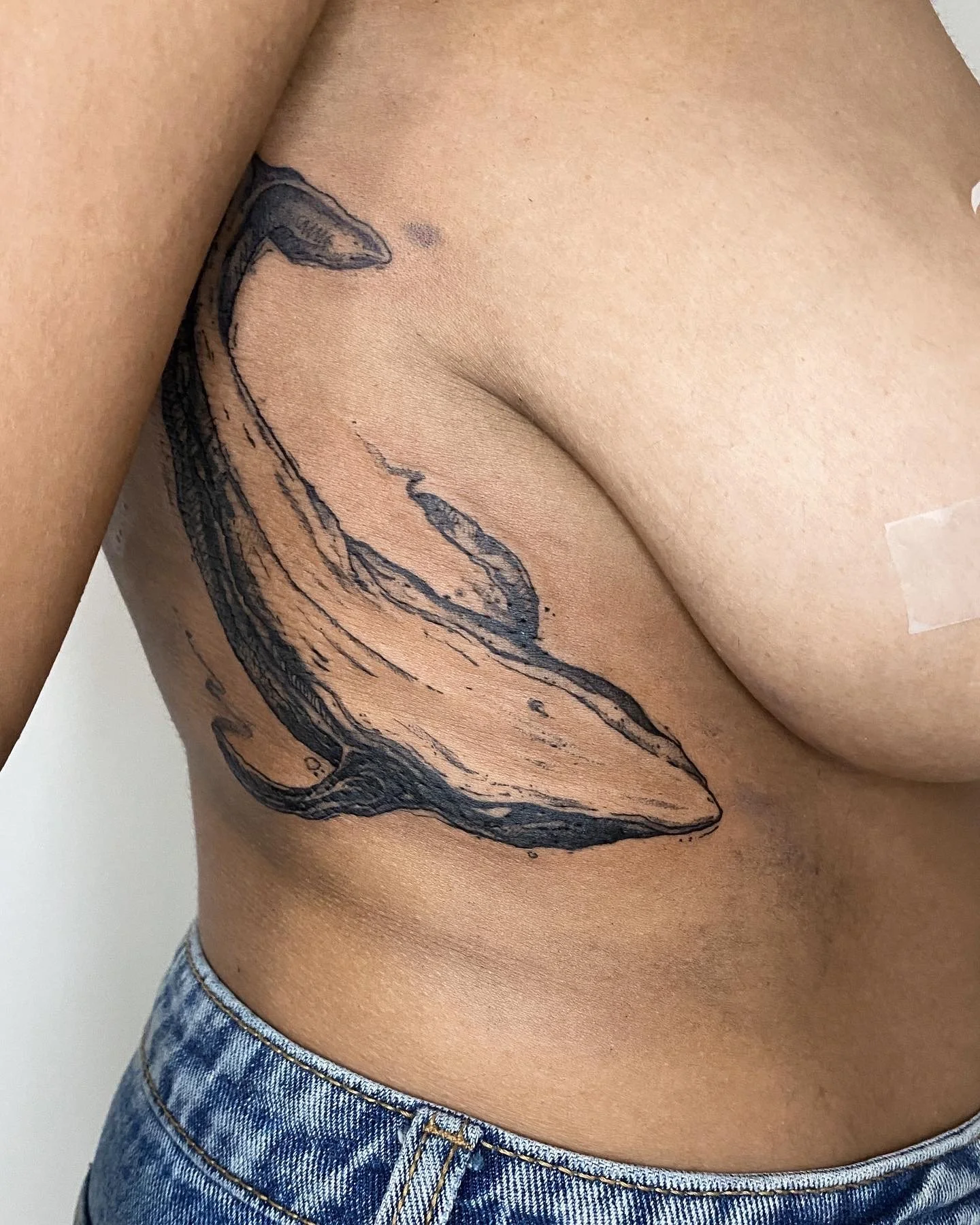 Tatouage d'une baleine noir sur le côté droit du corps d'une personne, portant un jean.