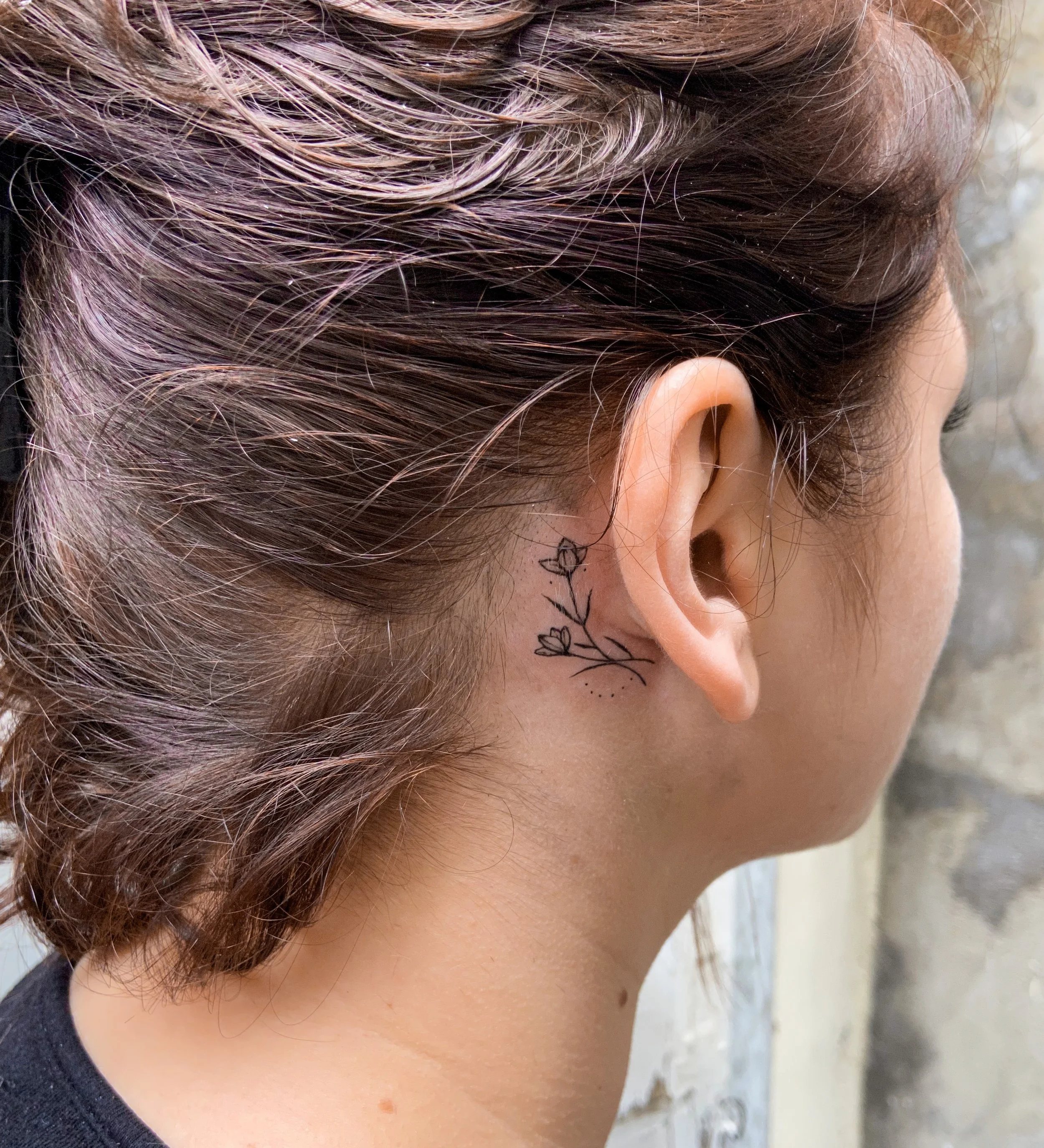 Vue rapprochée d'une oreille avec des cheveux brun clair et des reflets roses, tatouage floral sur le côté du visage