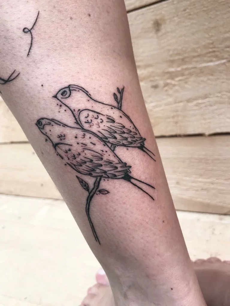 Tatouage de deux oiseaux perchés sur une branche, en style dessin au trait