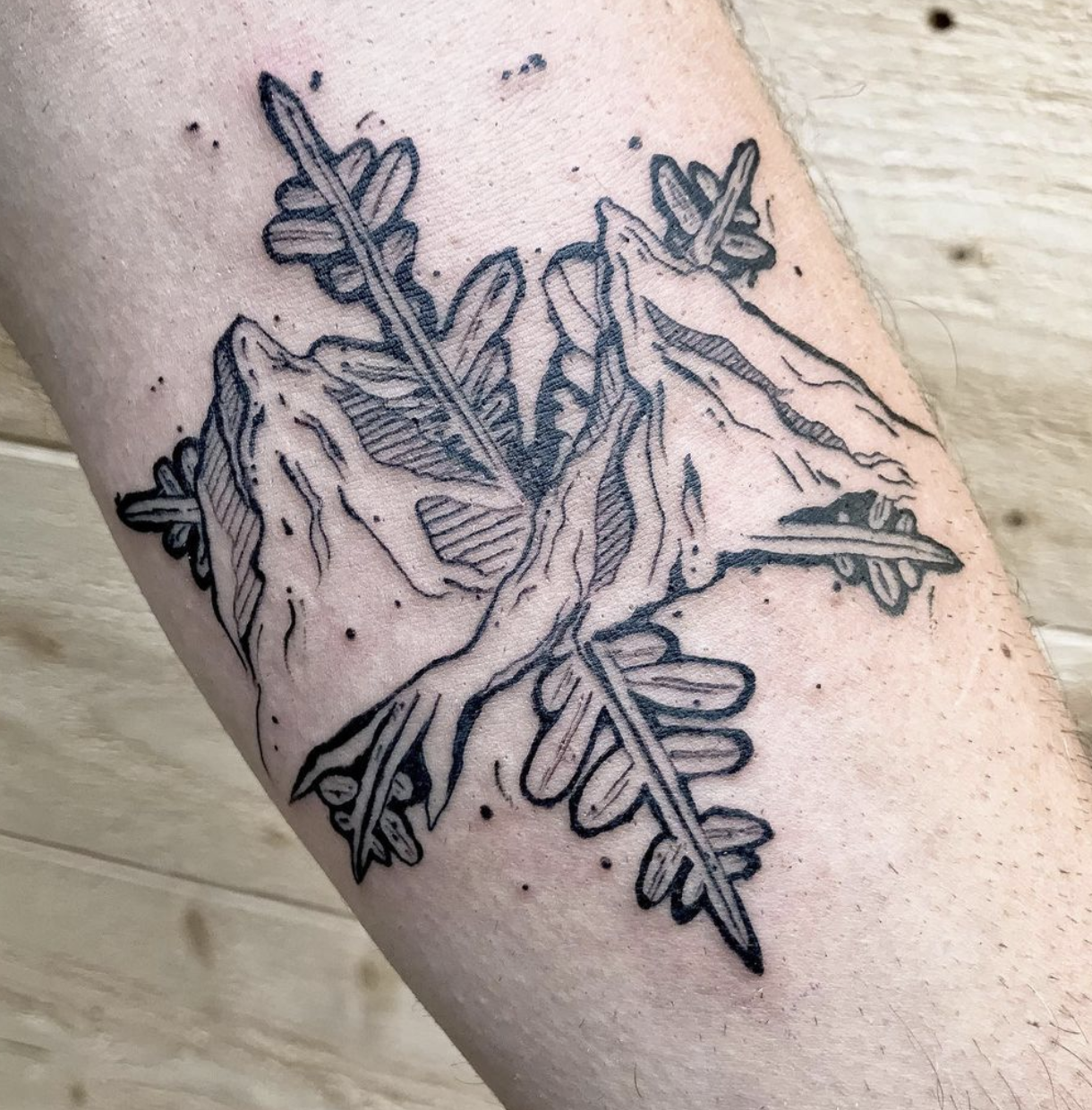 Tatouage en ligne d'une feuille d'érable avec de petites feuilles de pin, en noir et blanc.