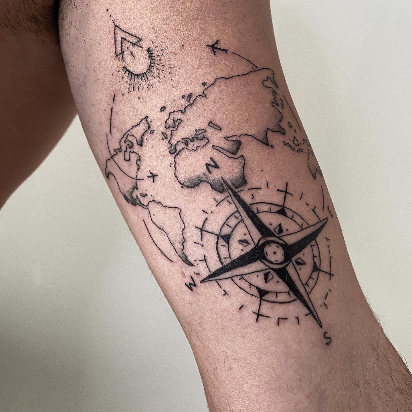 Tatouage d'une boussole, d'un globe terrestre avec des continents et une rose des vents.