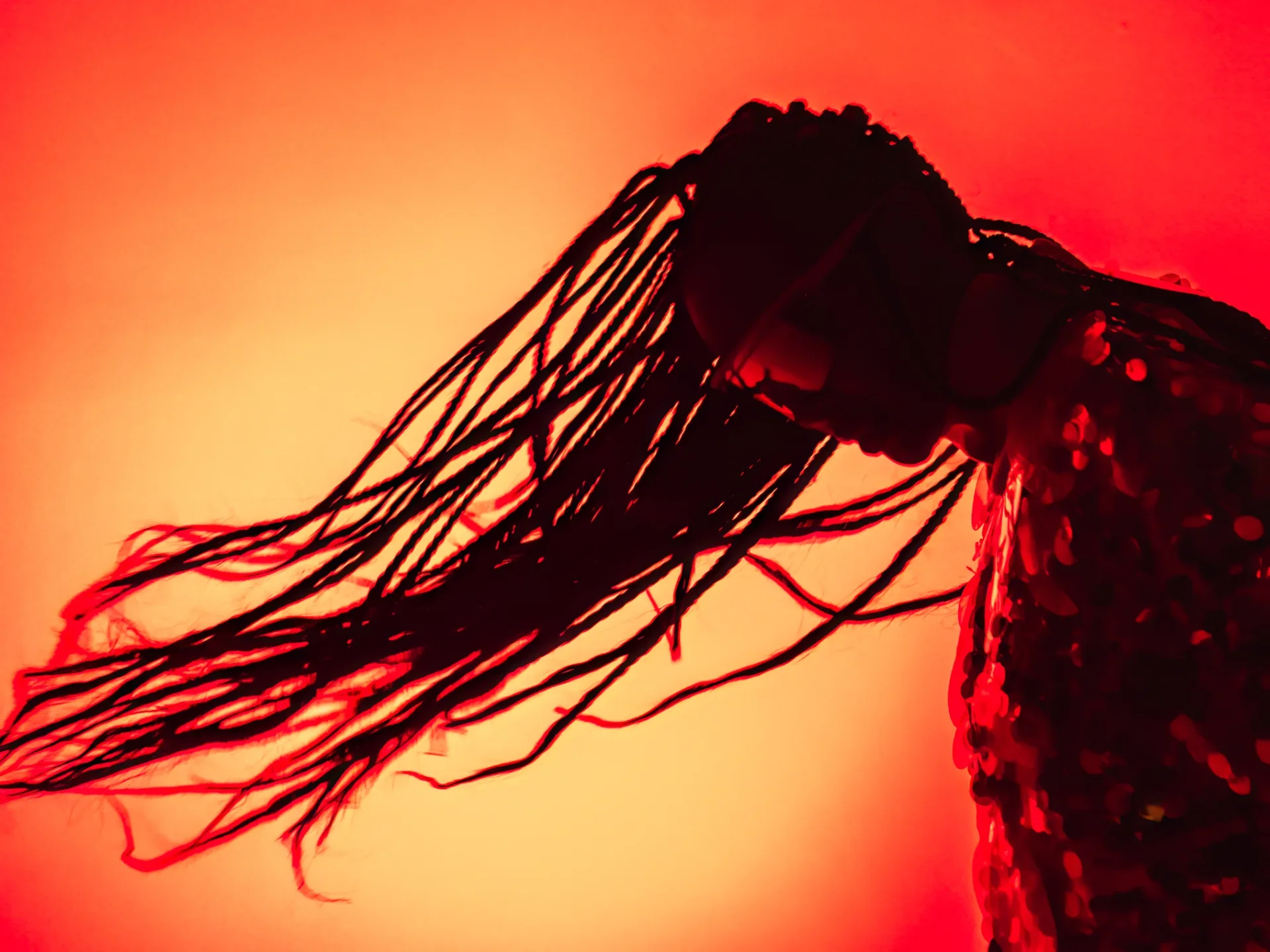 Silhouette of a person with long braids and a red floral dress against a red-orange background.