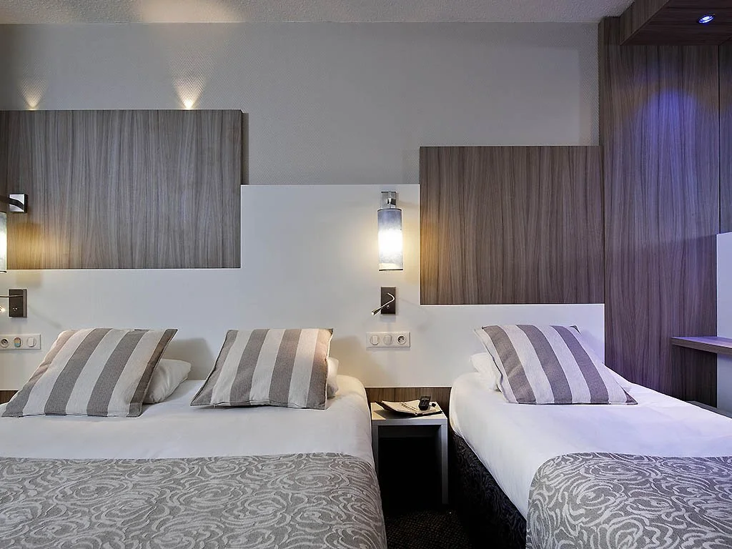 Chambre d'hôtel avec deux lits, oreillers rayés, lampes murales, et meubles en bois élégant.