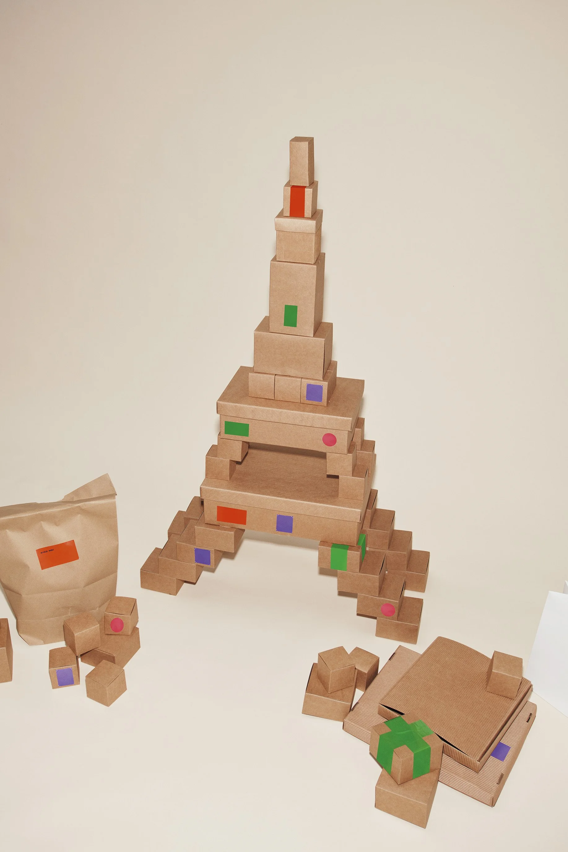 Une tour faite de boîtes en cartons de différentes tailles, décorée avec des autocollants colorés, formant une structure en forme de lettre 'A'.