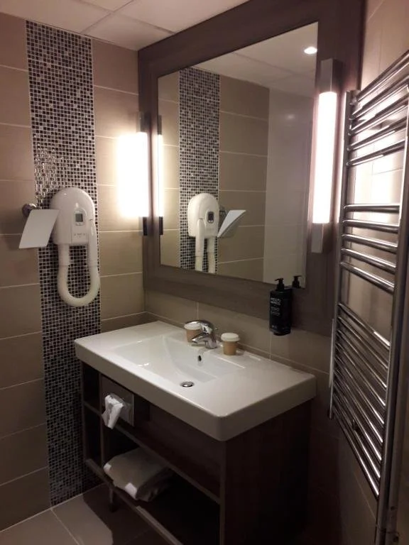 Toilettes avec lavabo, miroir, sèche-cheveux mural et radiateur électrique en acier inoxydable dans une salle de bain moderne.