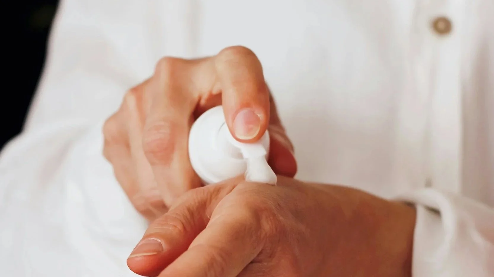Person applying lotion or cream to their arm from a white pump bottle.