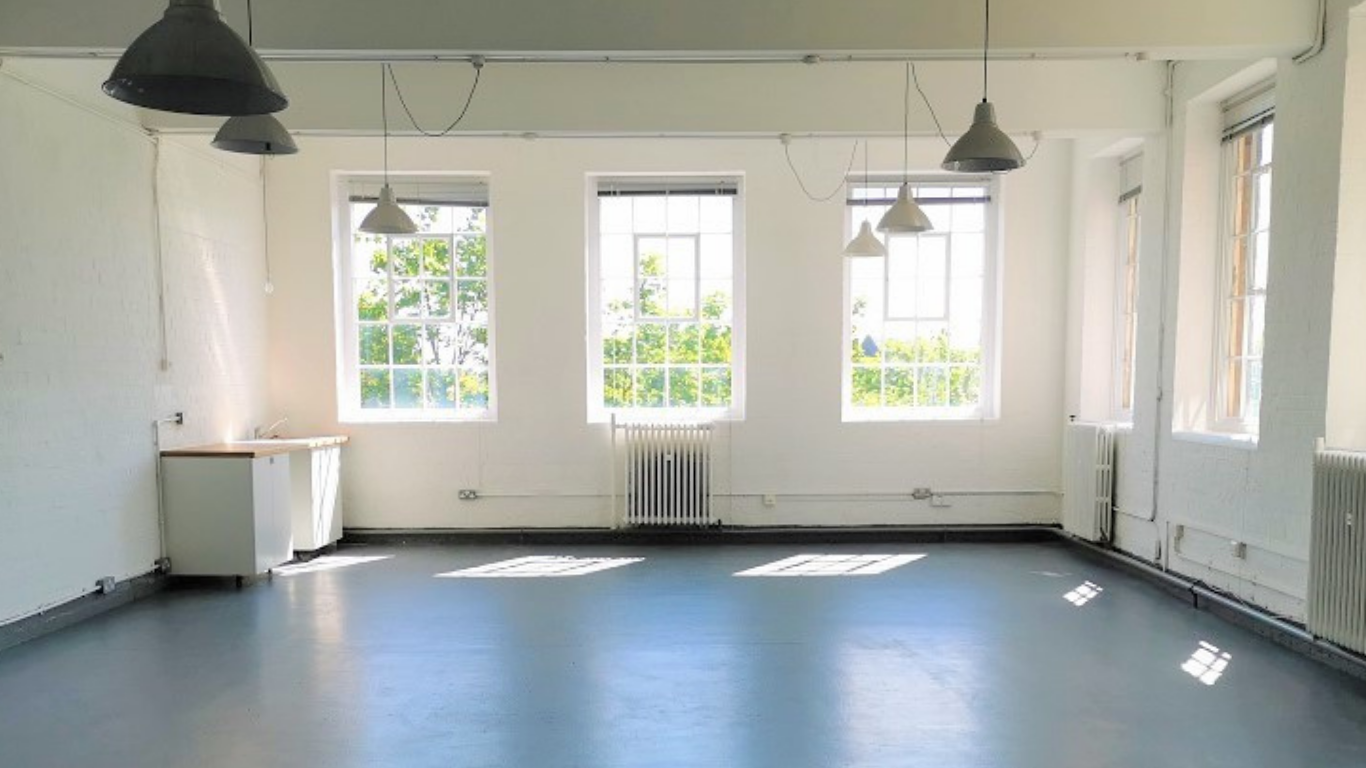 Empty studio with white walls, large windows, and hanging ceiling lights.