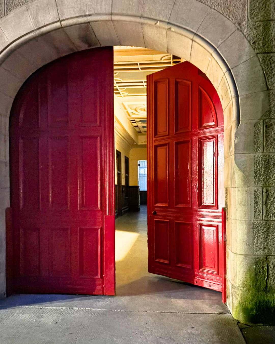 Open red wooden double doors leading into a room with a decorative ceiling and windows.