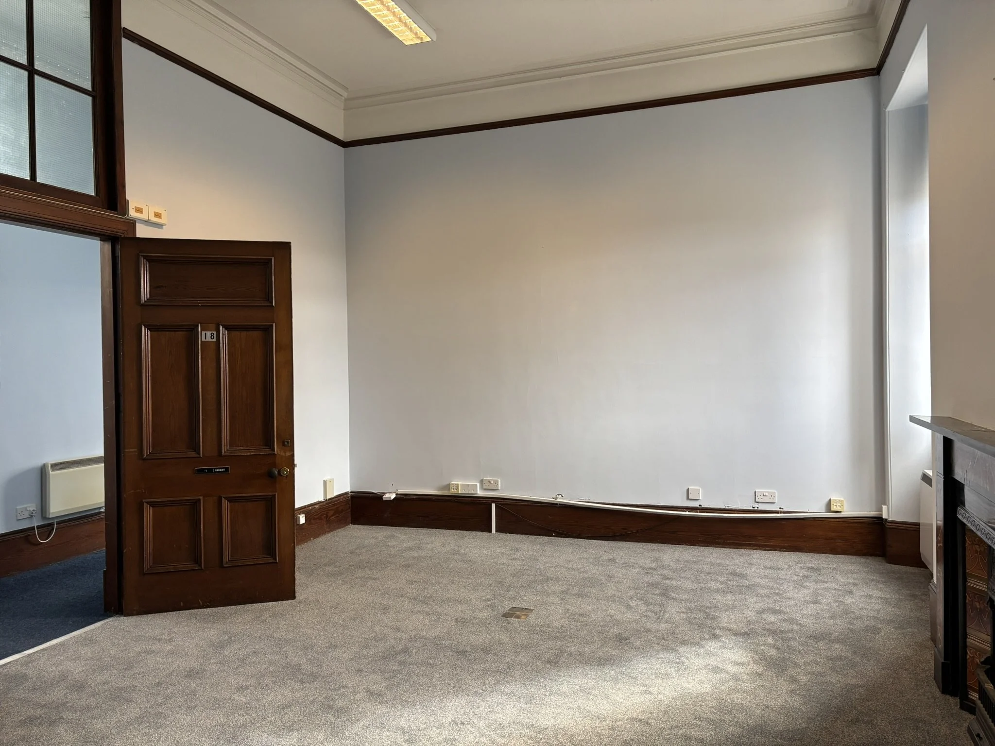 Empty room with wooden door, window, carpeted floor, and white walls.