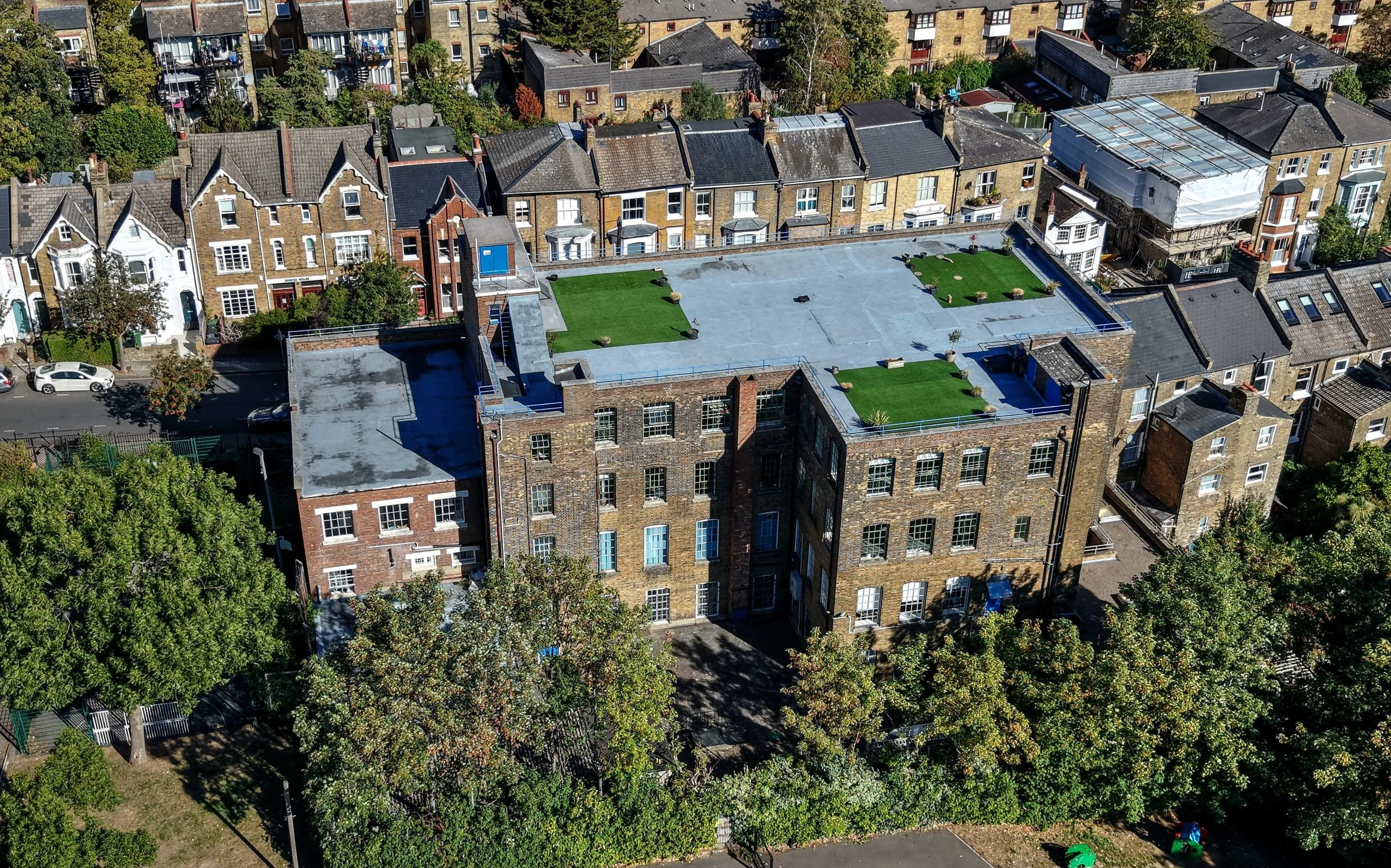 Drone shot of Archway Studis showing the surrounding neighbourhood and the artificial green lawn on the rooftop.
