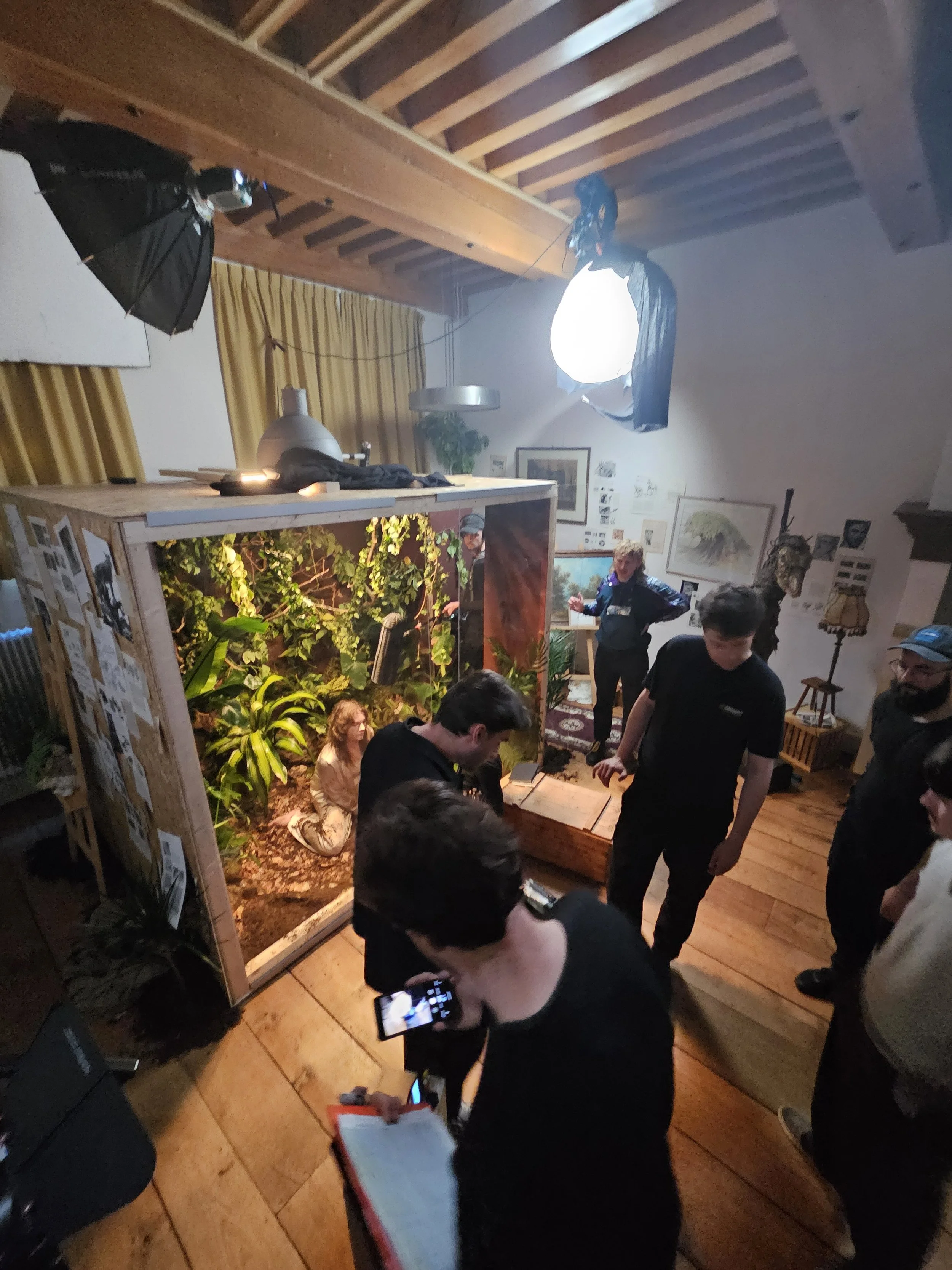 Een groepsfoto van mensen die binnen staan bij een presentatie of meetup, met een grote aquarium met veel planten en dieren, en een gepersonaliseerd display met foto's en informatie.