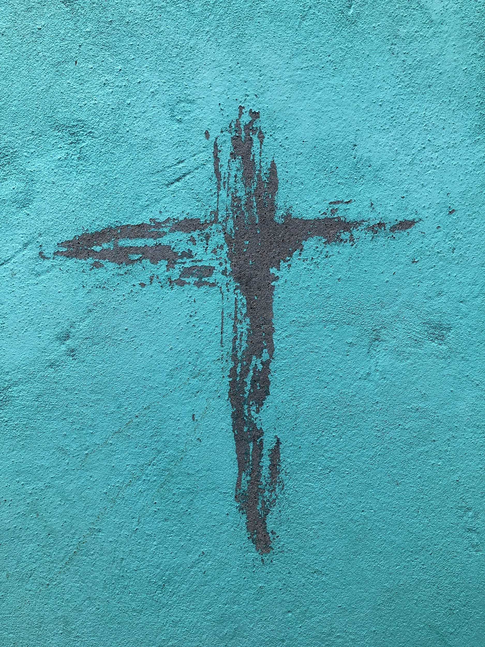 Black spray paint graffiti on a bright turquoise textured wall, forming an abstract shape resembling a person with outstretched arms.