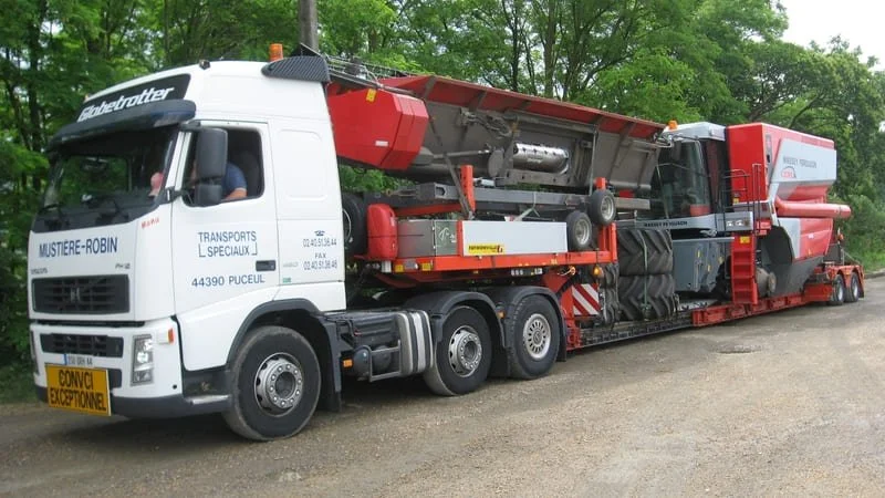 Un camion transporteur de machines industrielles stationné sur un chemin bordé d'arbres.