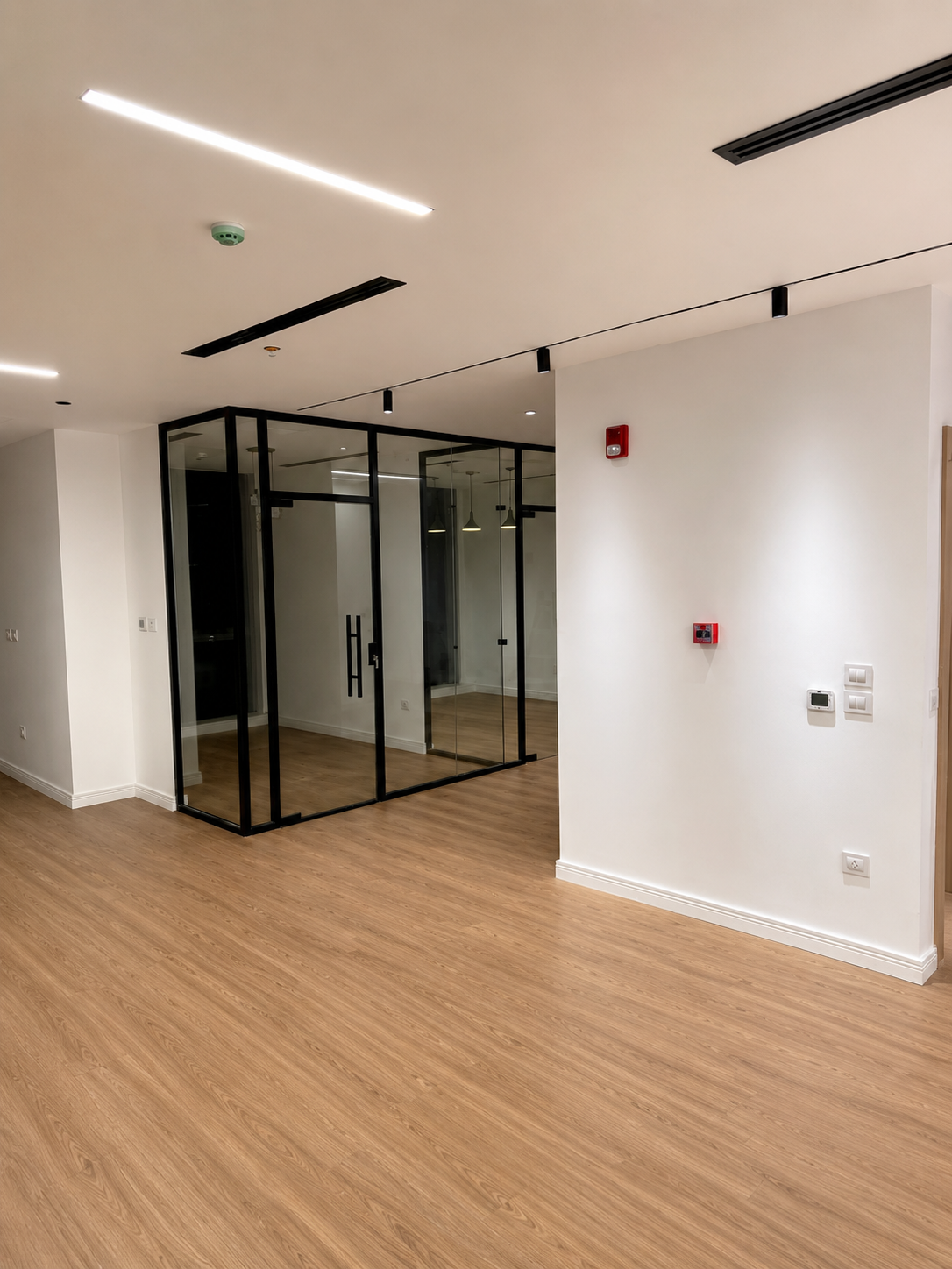 Empty room with wood flooring and a glass enclosed office space with black metal framing.