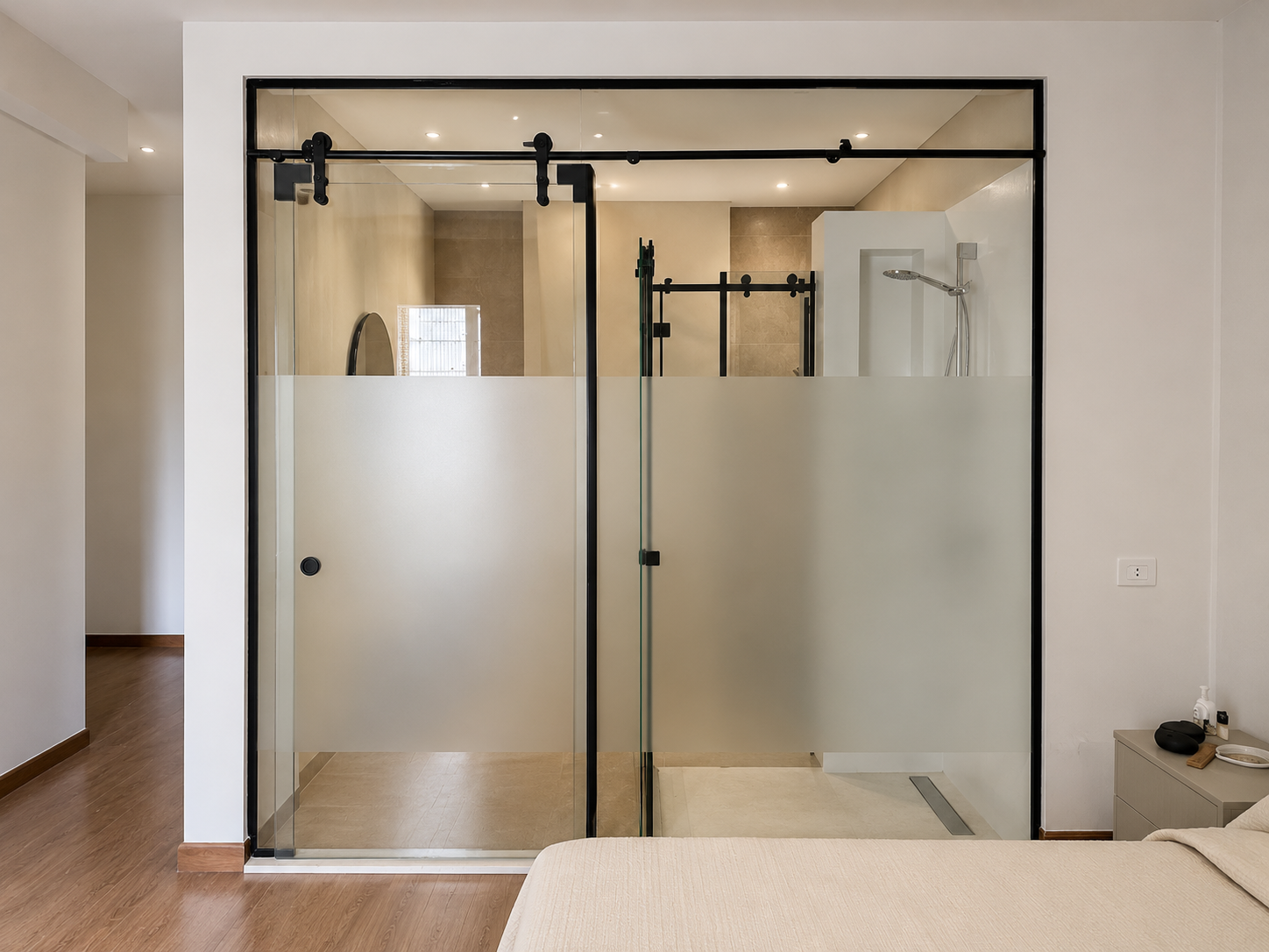 Modern glass bathroom shower enclosure with frosted lower panels and a black sliding barn door, mounted on a black track, in a minimalist bedroom setting.