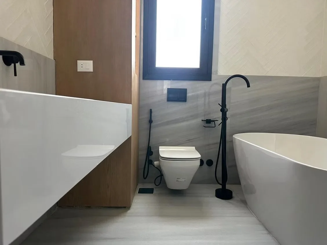 Modern bathroom with a freestanding bathtub, wall-mounted toilet, black fixtures, and a window.
