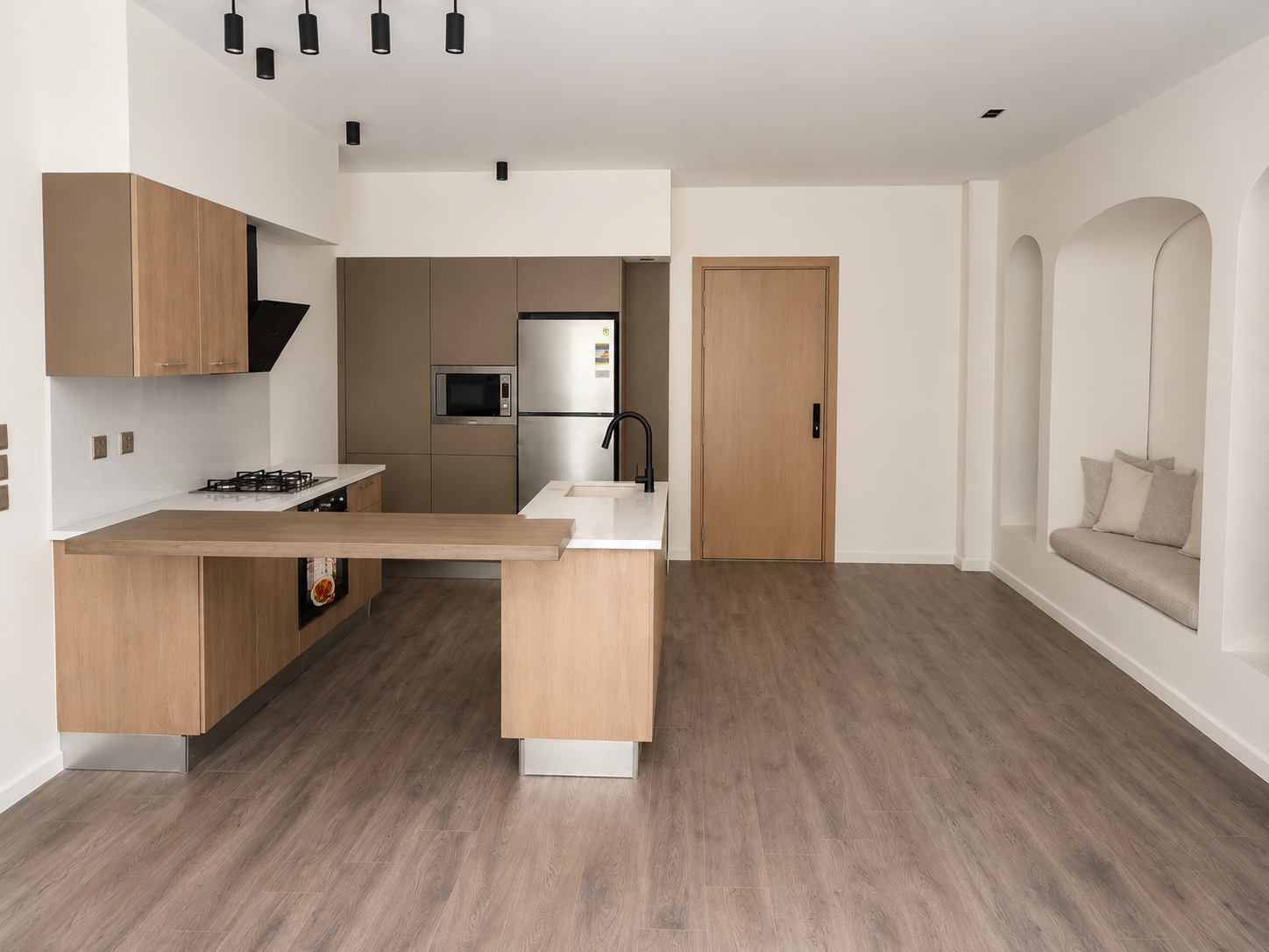 Modern kitchen with wooden cabinets, a white countertop, and stainless steel appliances, including a refrigerator and microwave, with a wooden sliding door to the right and a built-in seating nook with cushions on the wall.