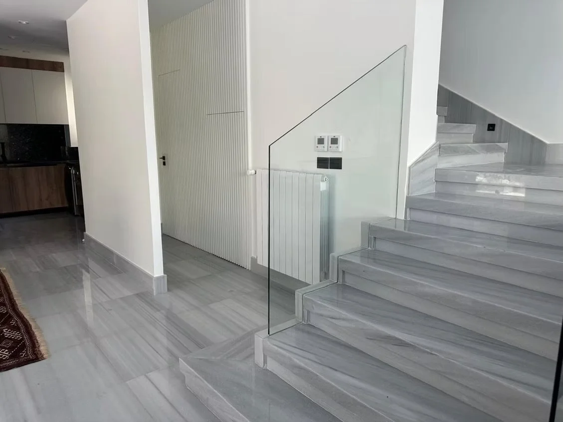 Modern interior with marble staircase, glass railing, a radiator, and digital controls on the wall.