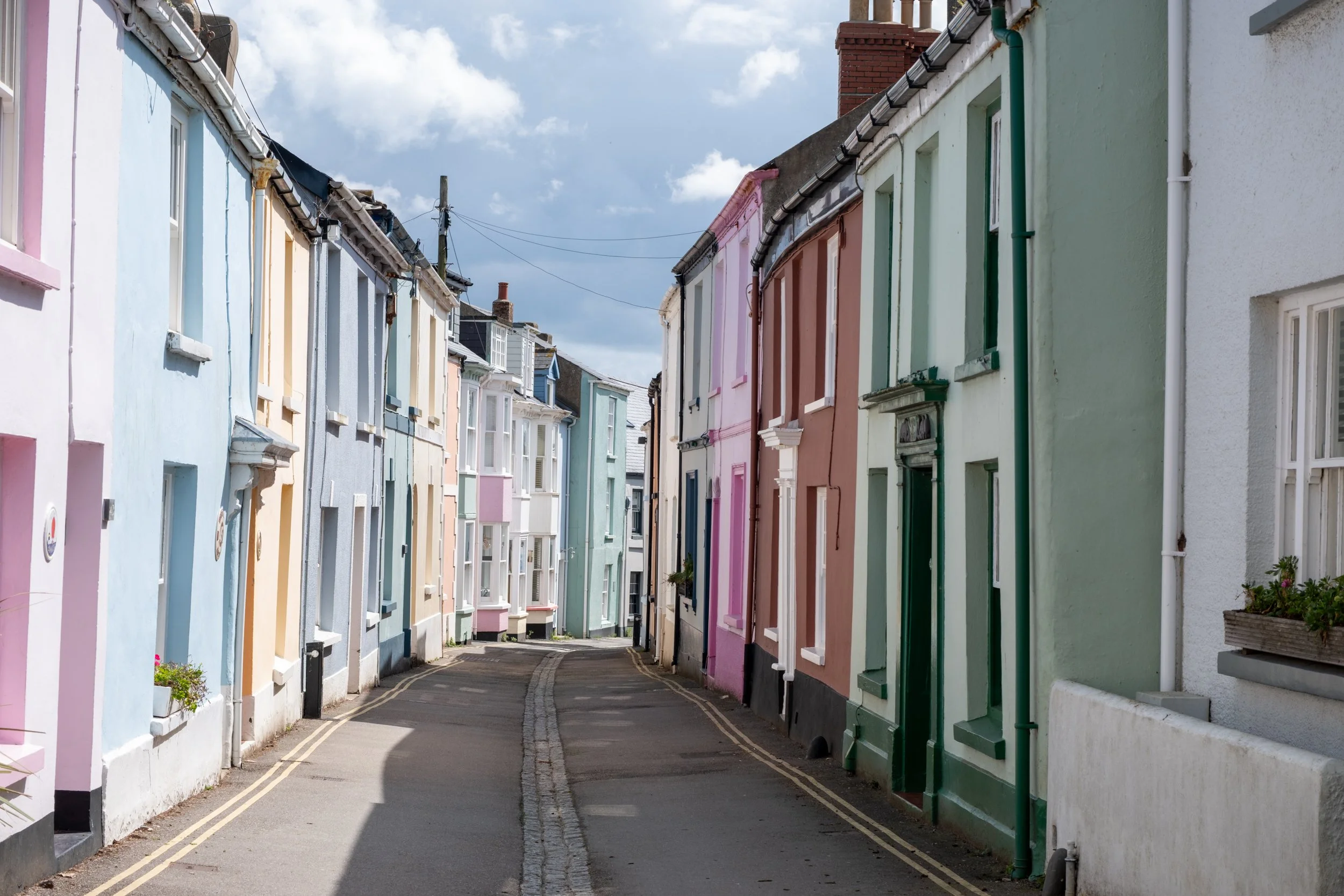 Colorful houses lining a narrow curved street, painted in pastel shades including pink, blue, and green, with a cloudy sky above.