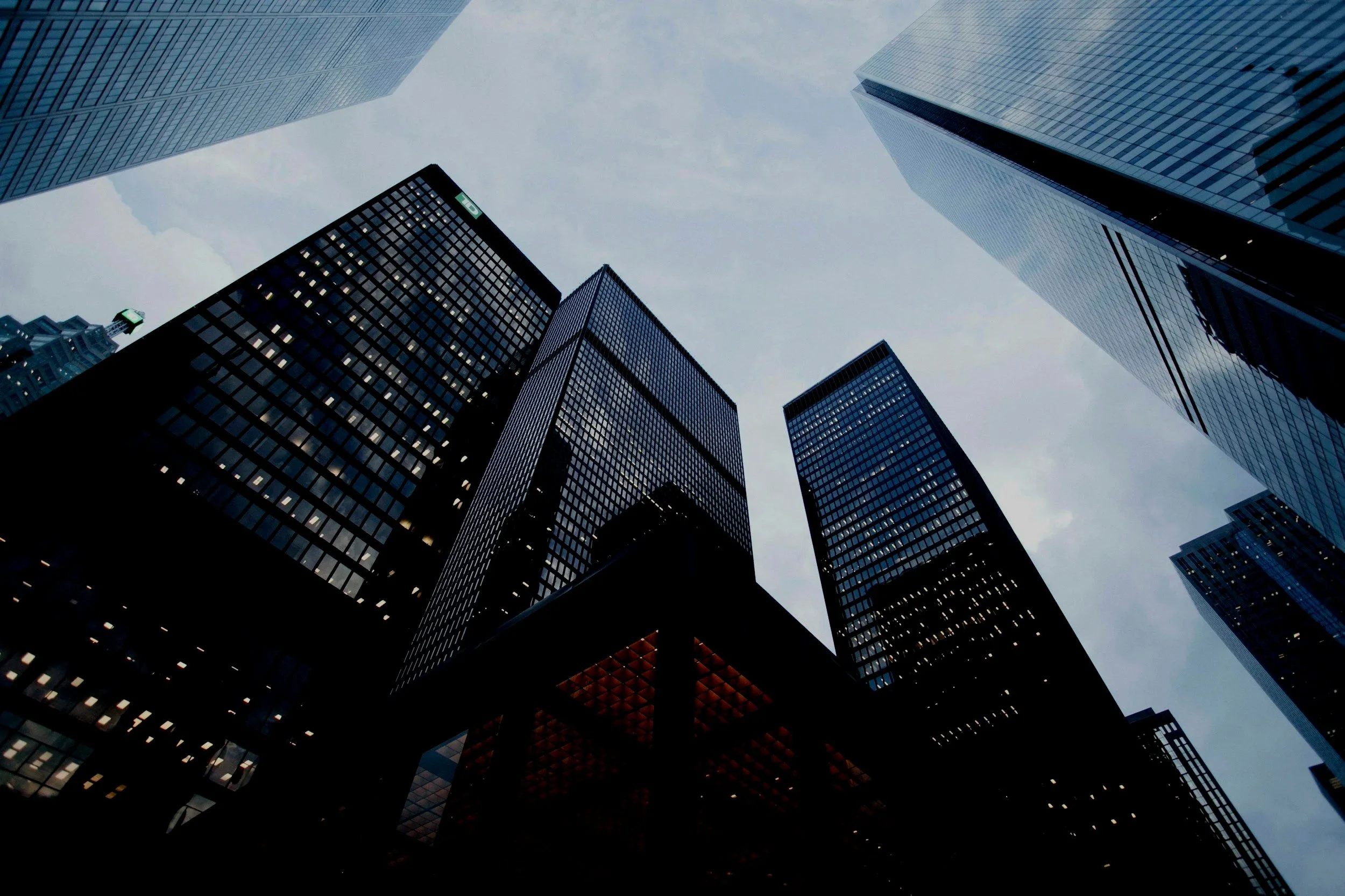 View looking up at tall skyscrapers in a city with glass facades reflecting the sky.