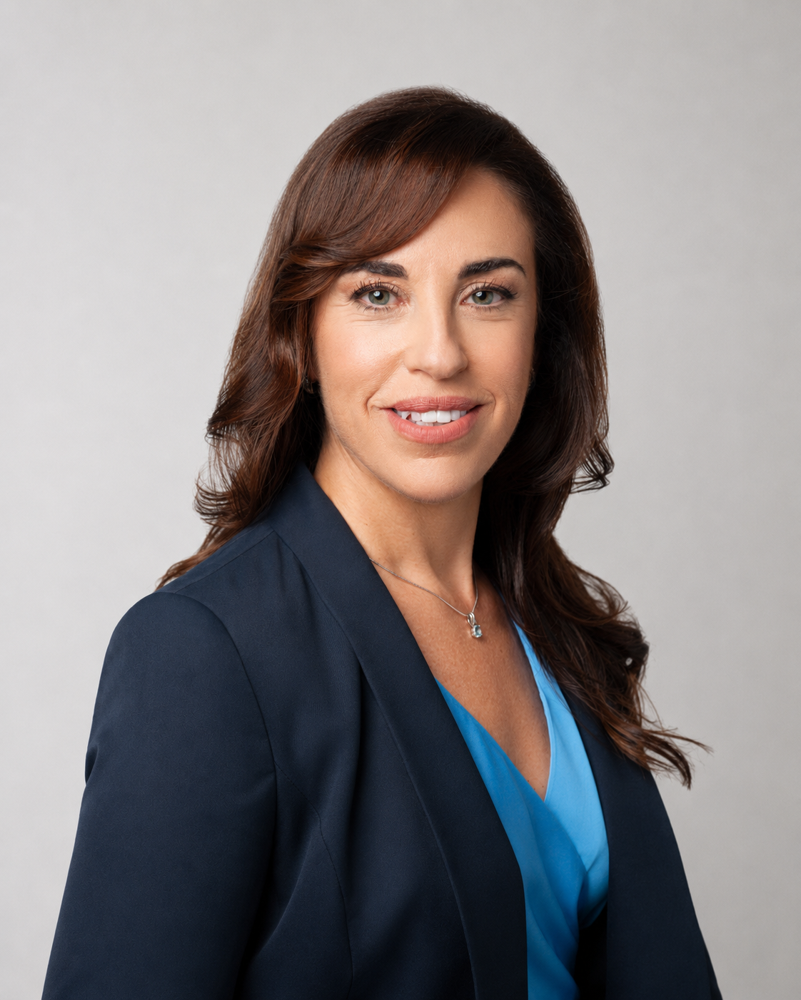A professional woman with brown hair styled in loose waves, wearing a navy blazer and a blue blouse, smiling at the camera.