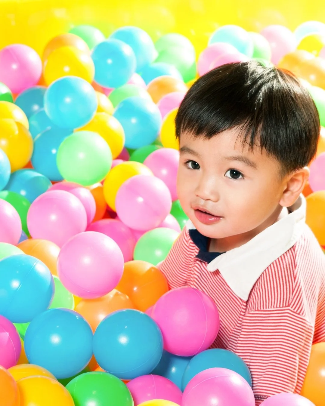 Young boy playing in a colorful ball pit with pink, blue, green, and yellow plastic balls.