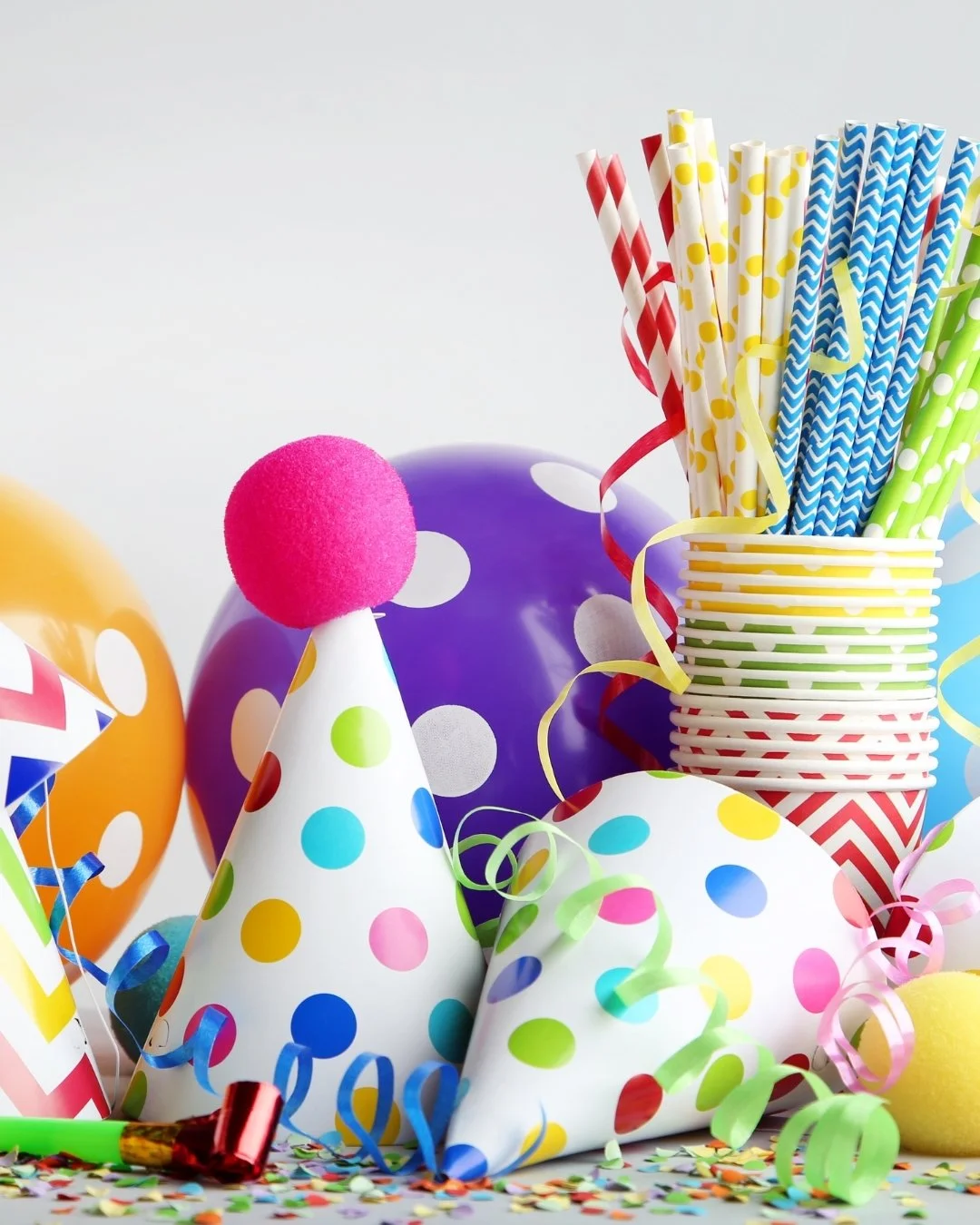 Colorful birthday party hats, balloons, paper straws, and confetti.