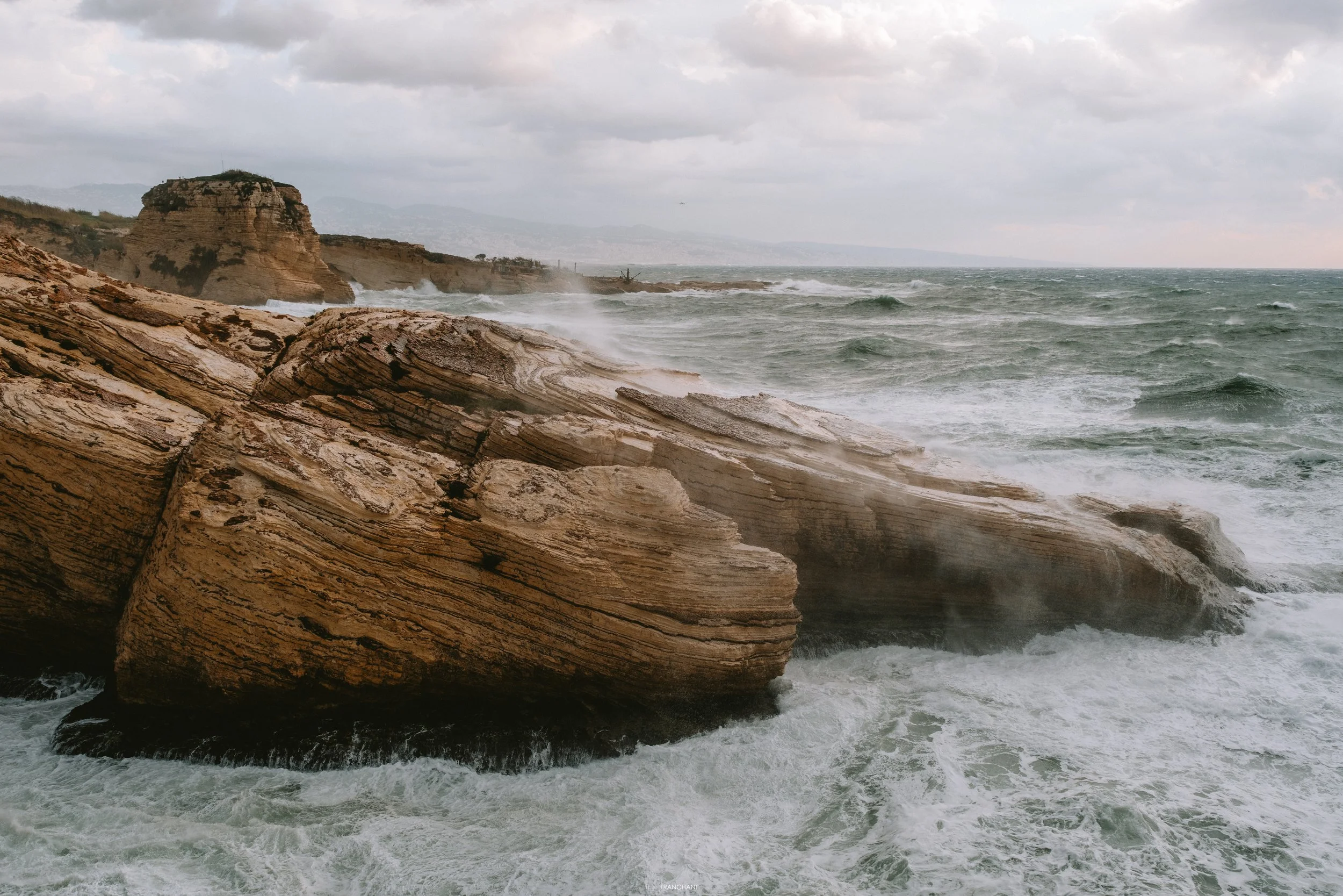 Stormy ocean waves crashing against rocky cliffs on a cloudy day.