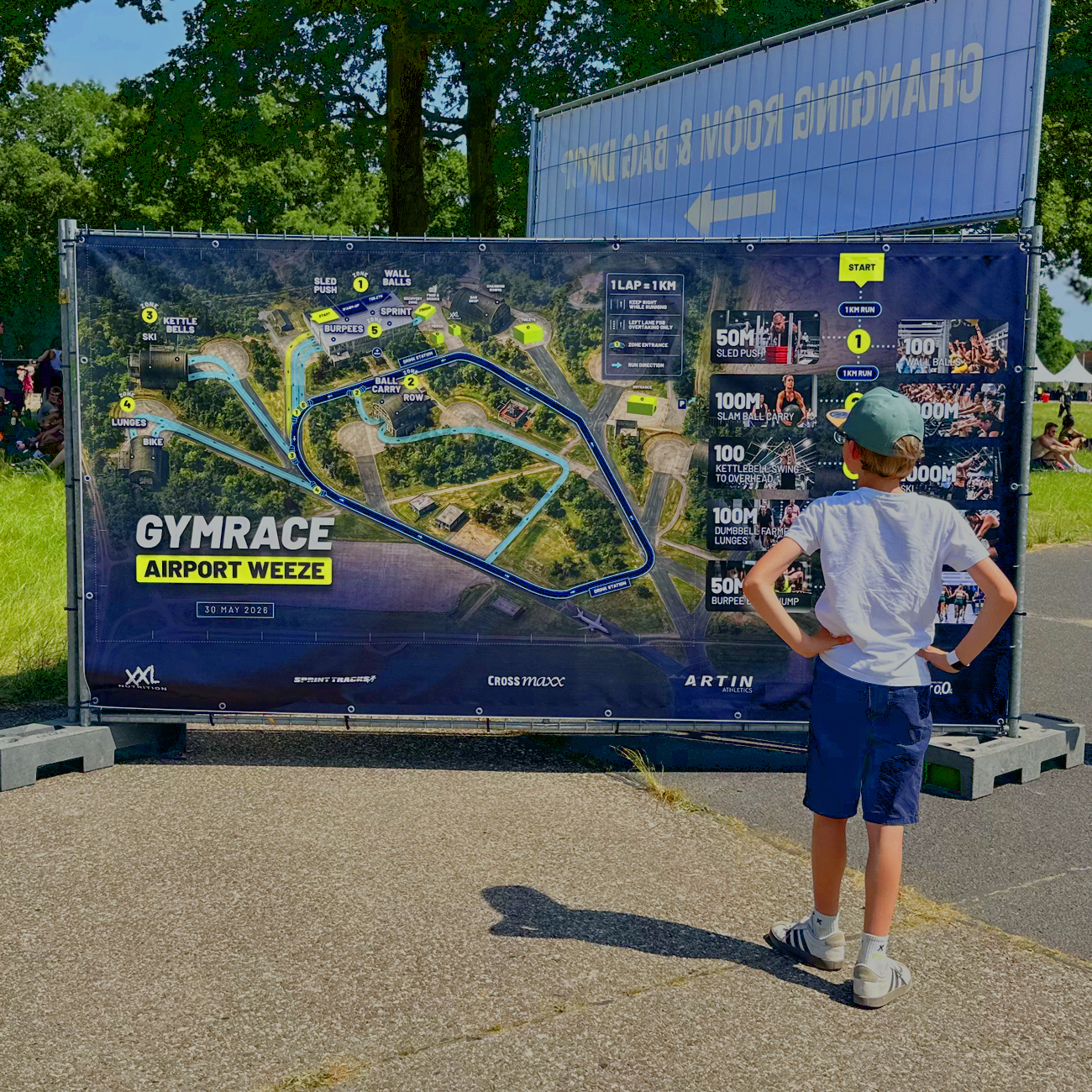 Omgevingskaart van het sportevenement Gymrace op luchthaven Weeze, met een route en instructies voor verschillende oefenstages. Een jongen kijkt naar de kaart.