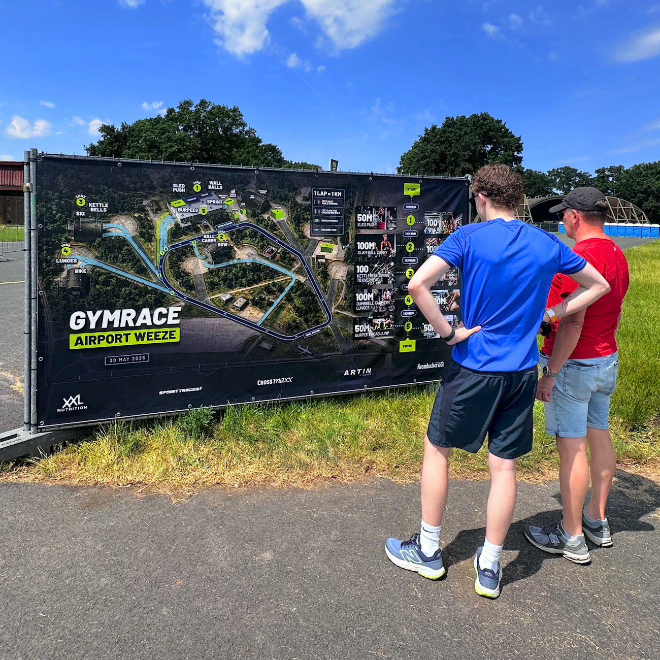 Twee mannen bekijken een plattegrond van een mountainbike-parcours genaamd GymRace bij Airport Weeze op een zonnige dag.