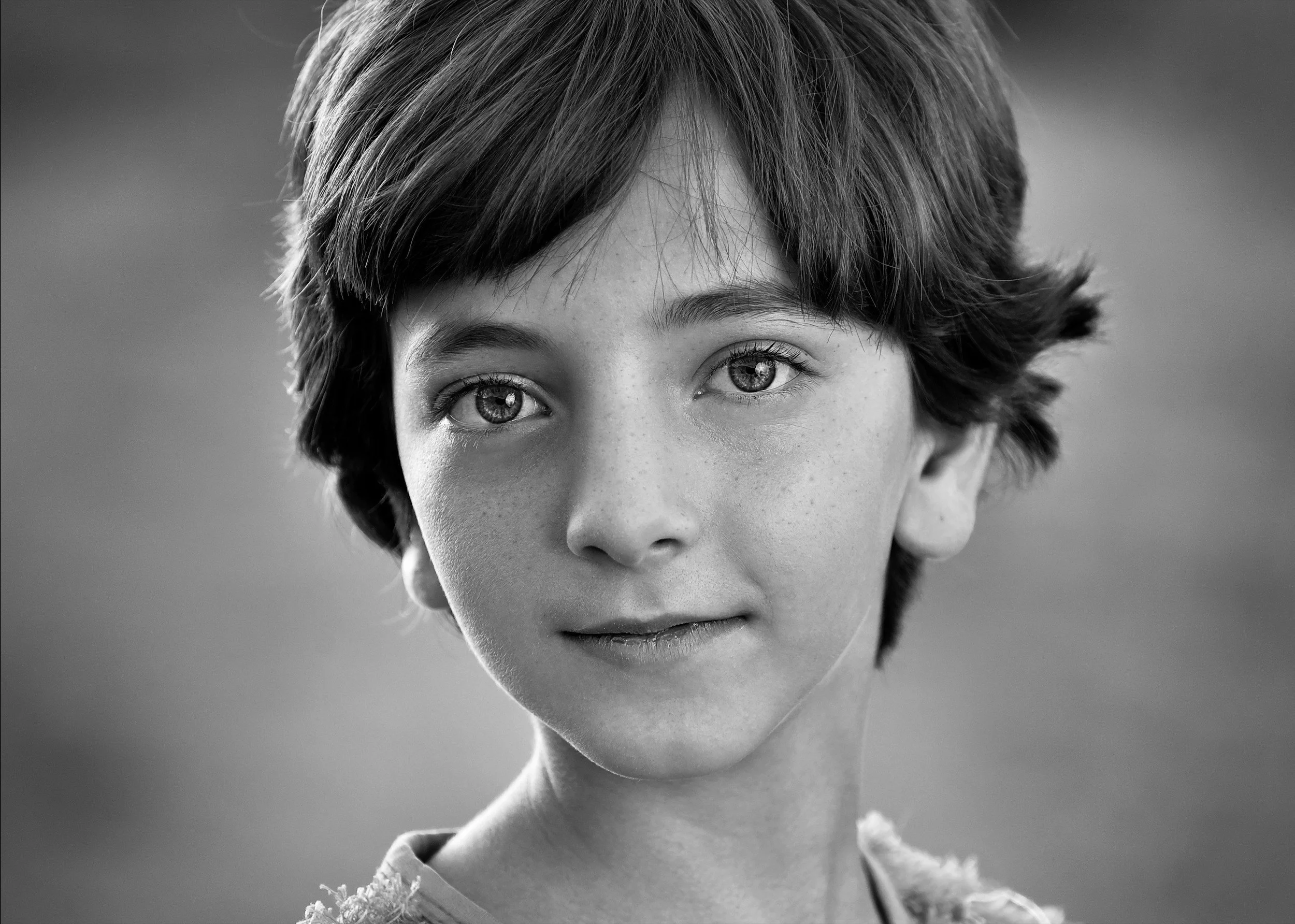 Close-up black-and-white portrait of a young woman with short, tousled hair and expressive eyes, looking slightly upward.